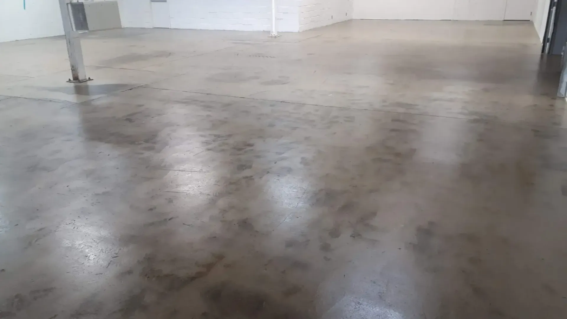 Concrete floor in an empty room, reflective and wet looking, with support columns visible.