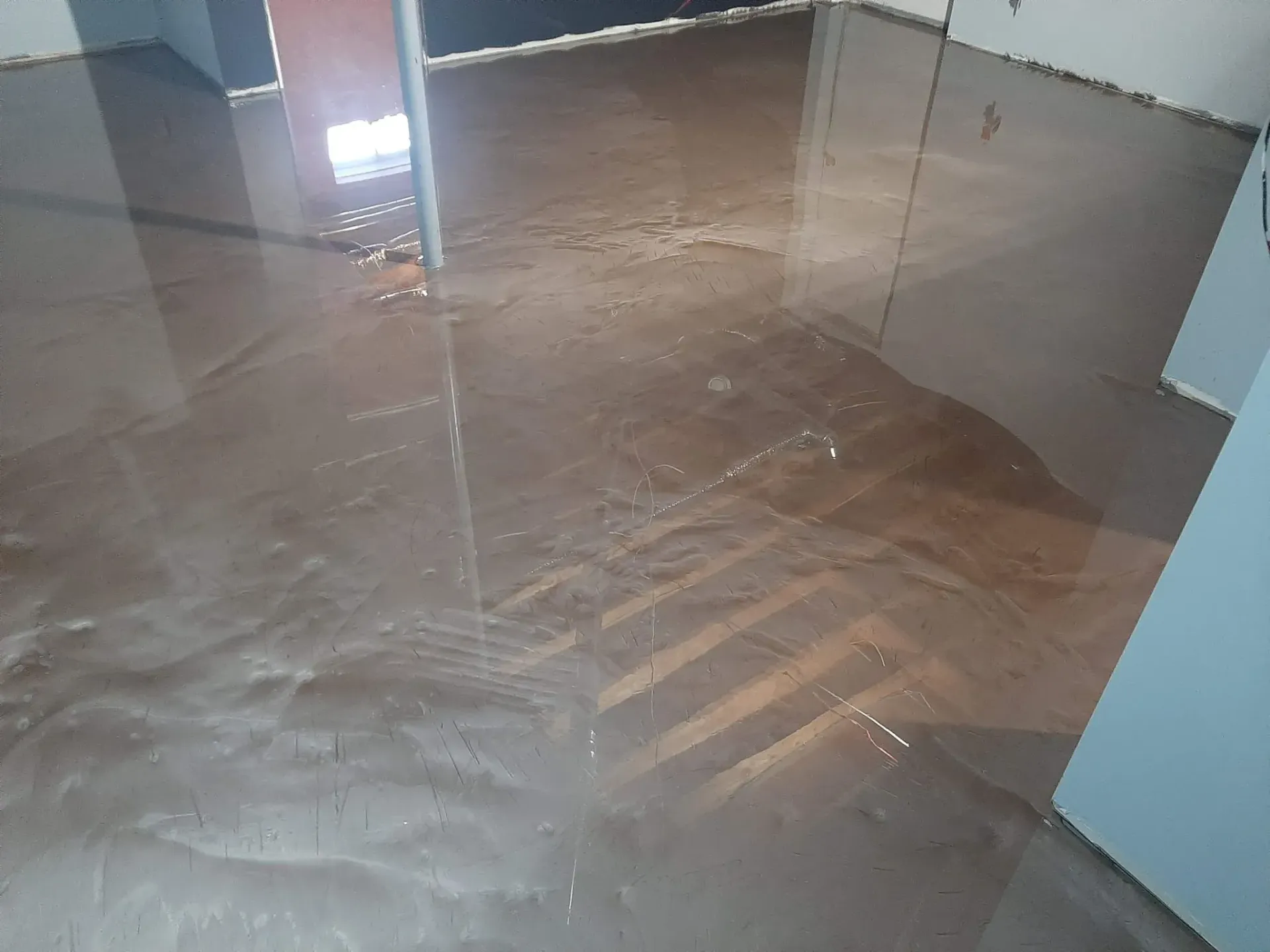 A room with a flooded floor and a reflection of a window.