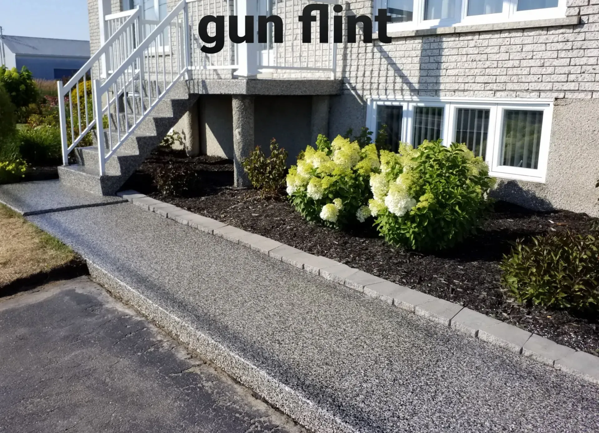 Path made of small gun flint stones leads to a house with white stairs, flanked by flower beds.