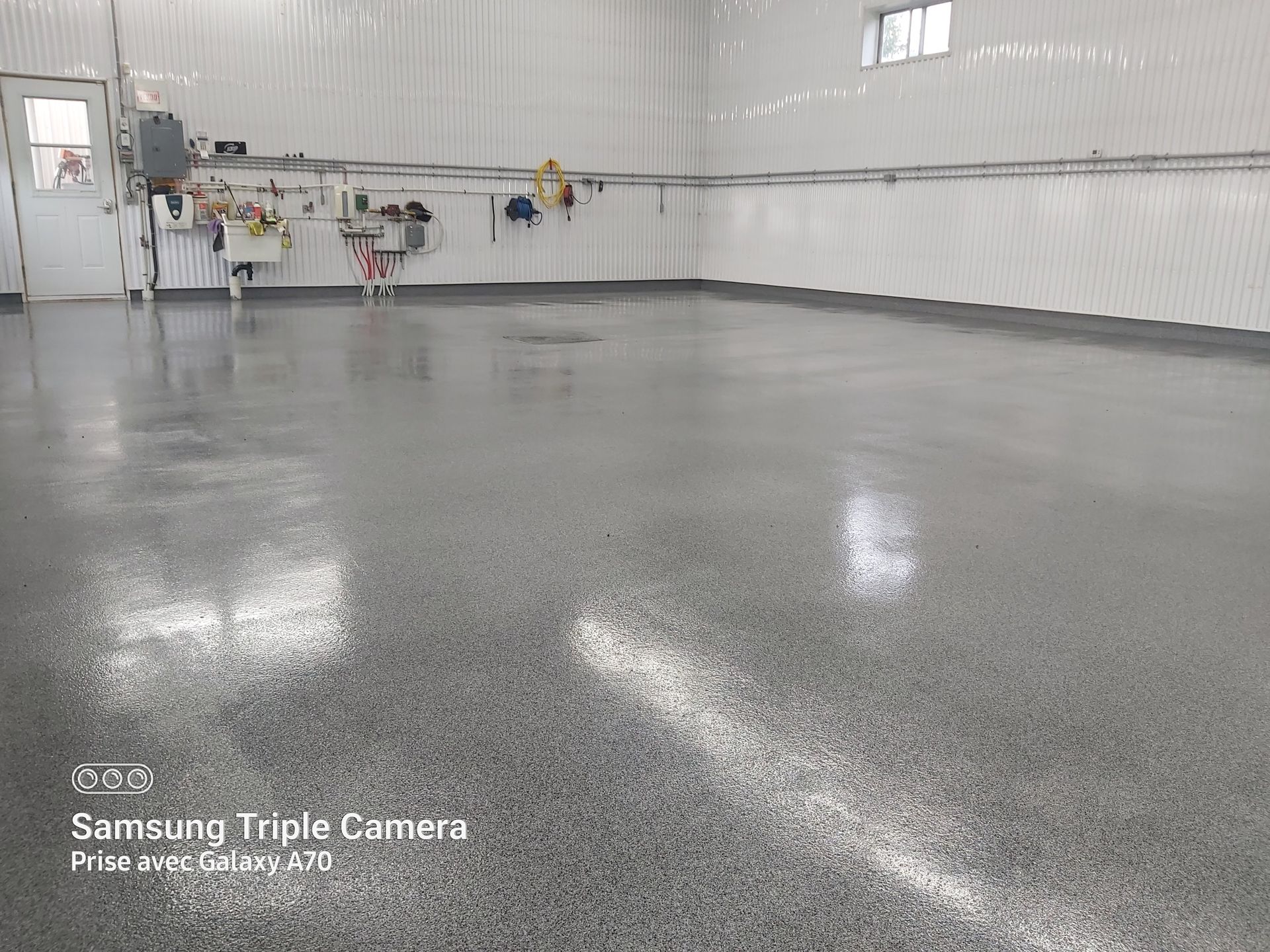A wide, shiny, gray epoxy-coated floor in a white-walled industrial space with a sink and tools in the background.