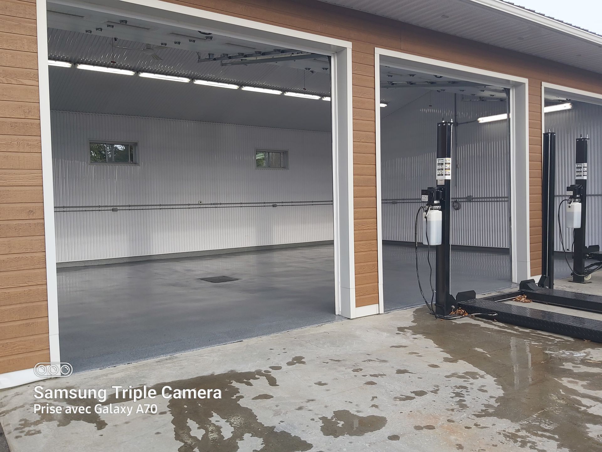 Three open garage bays with gray floors, white walls, and vehicle lifts. Brown exterior trim.
