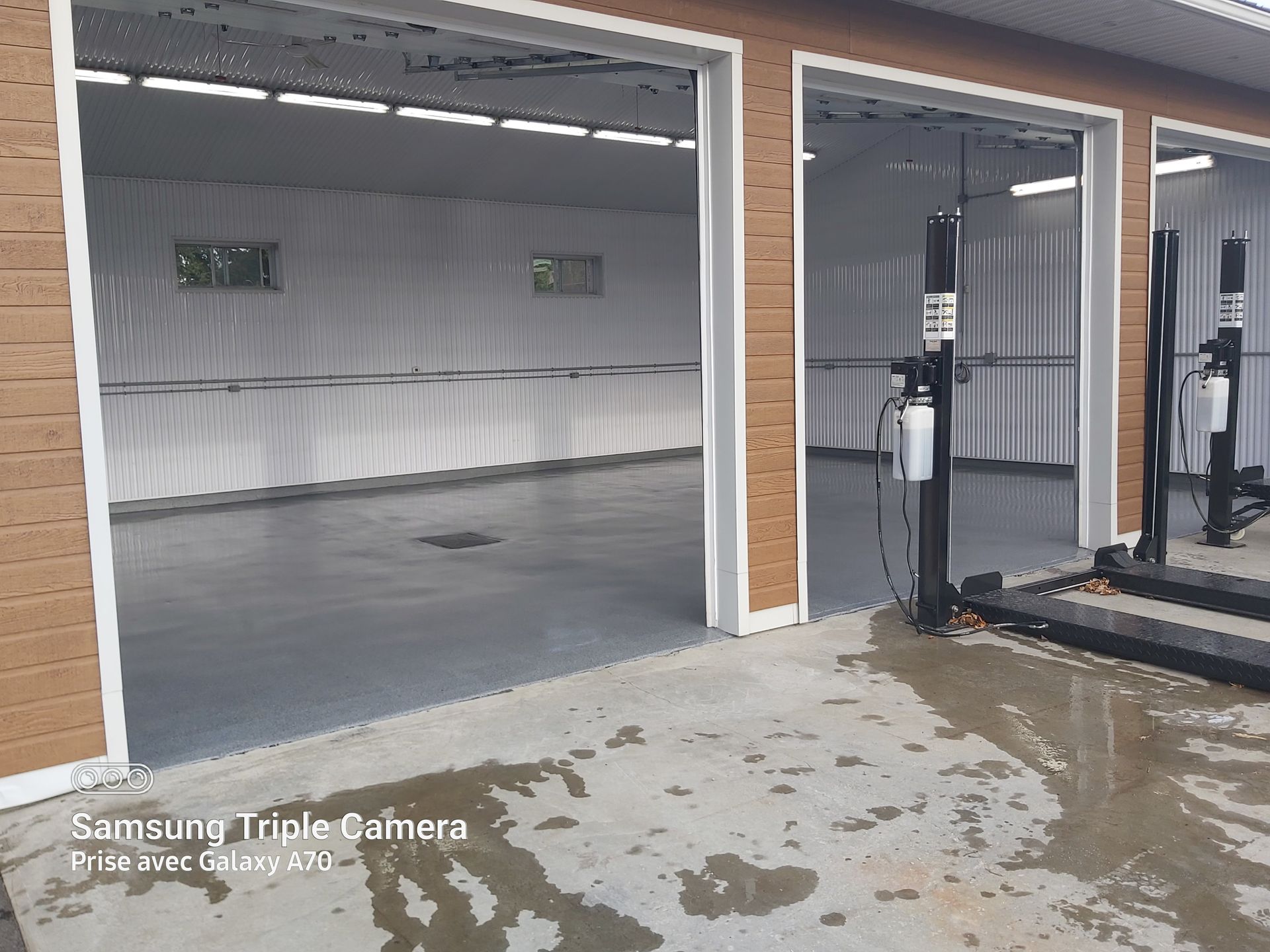 Three open garage bays with lifts, gray concrete floors, and corrugated white walls.