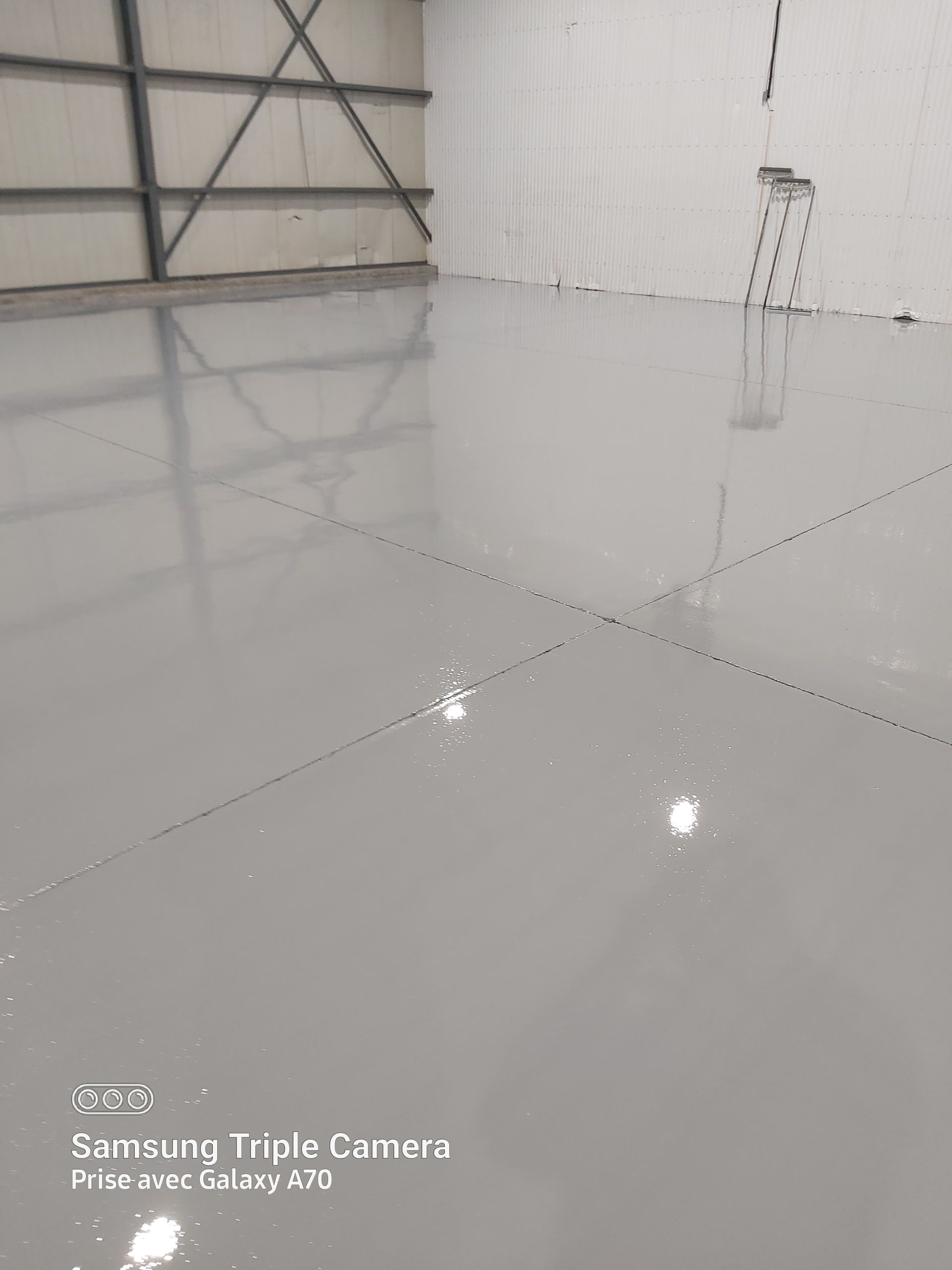 Grey epoxy floor in a large, empty warehouse with metal supports, ladder, and white walls.