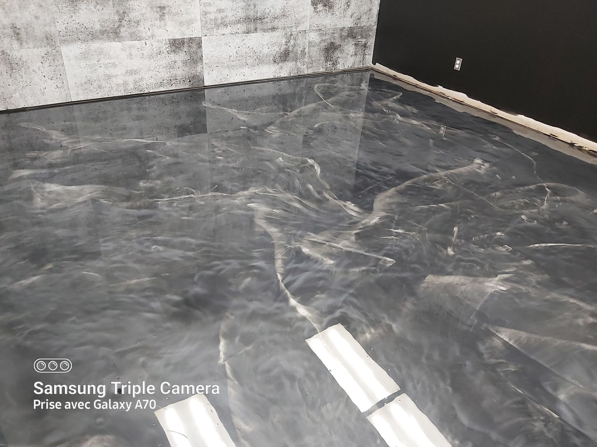 Shiny gray epoxy floor with marble-like swirls, next to a textured white-gray wall.