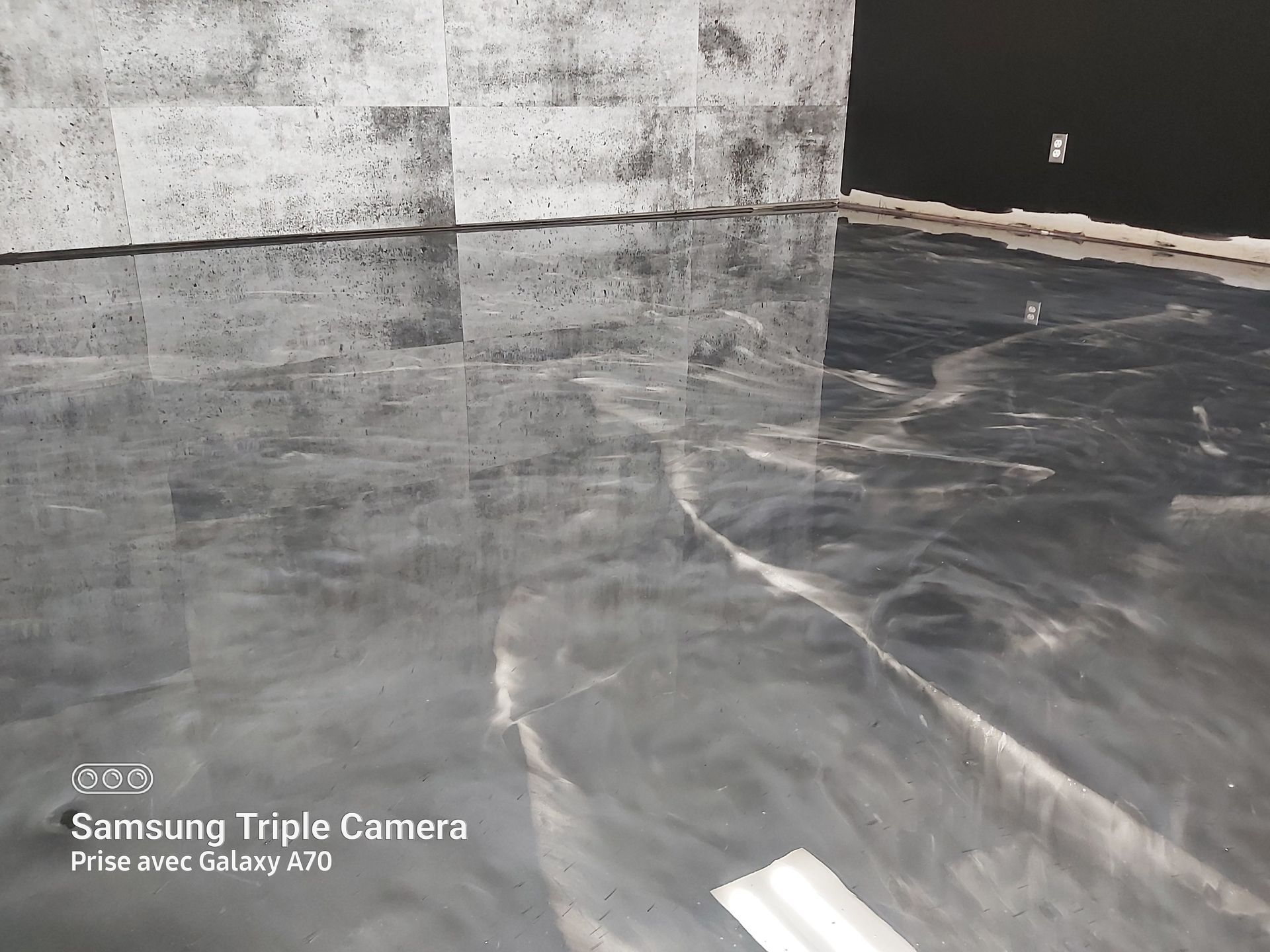 Gray epoxy floor reflecting light, with gray stone wall in the background.