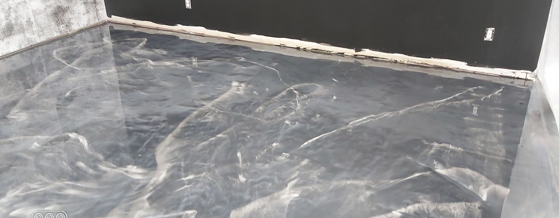 A glossy, gray and white marble-patterned epoxy floor in a room under construction with dark baseboards.