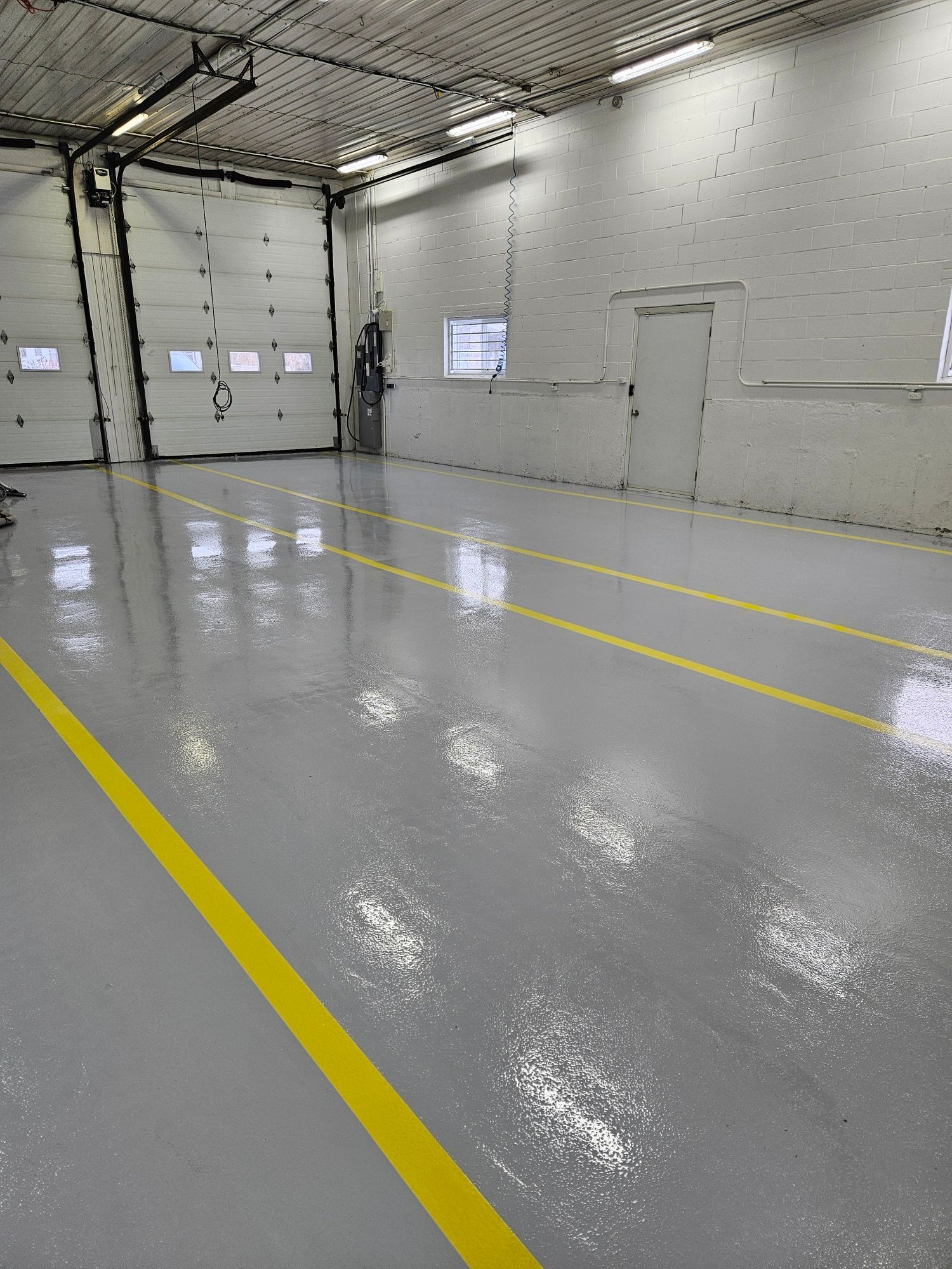 A gray, glossy warehouse floor with yellow lines. A garage door is open at the back.