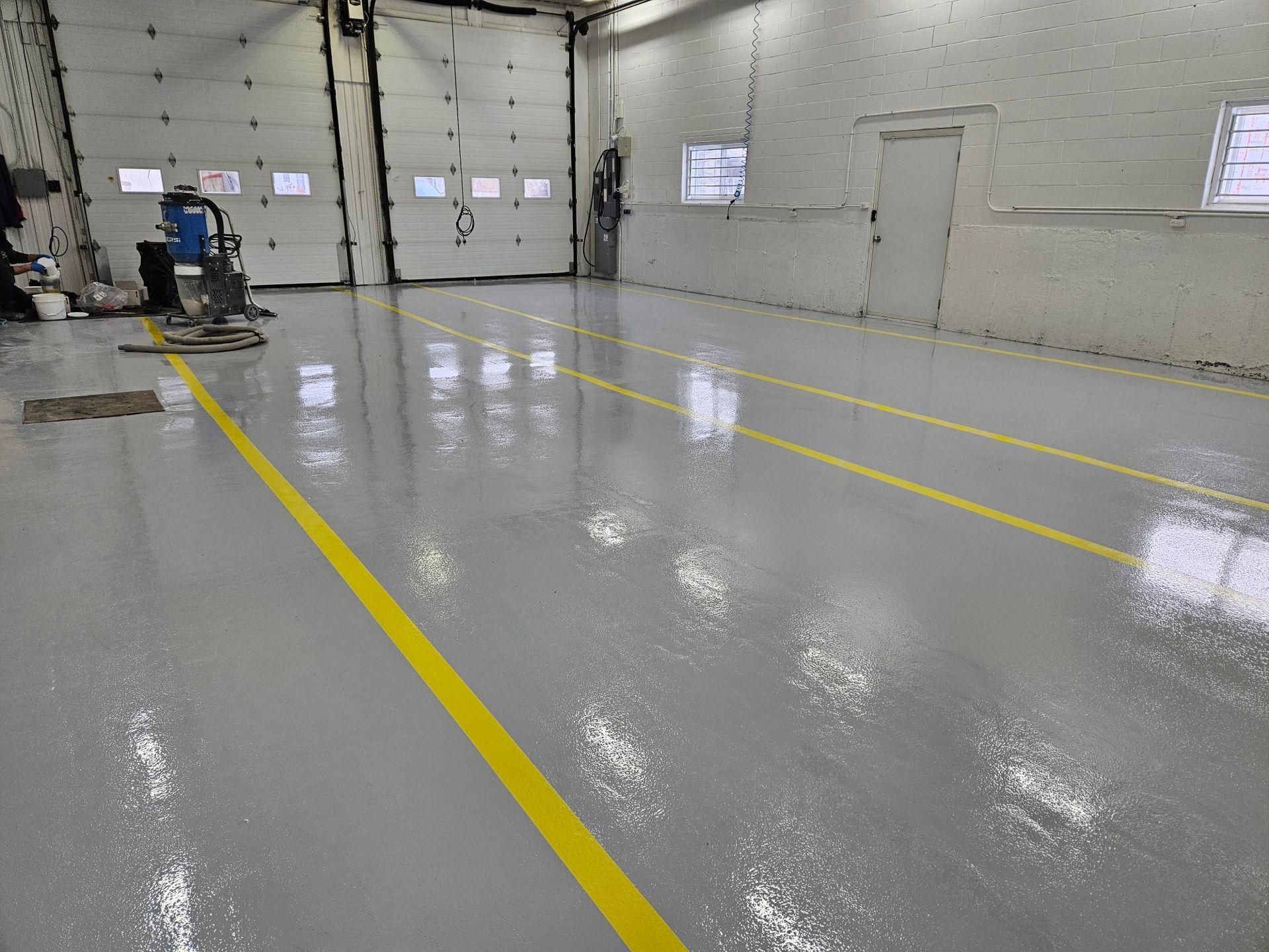 Gray industrial floor with yellow lines, in a white-walled building with garage doors.