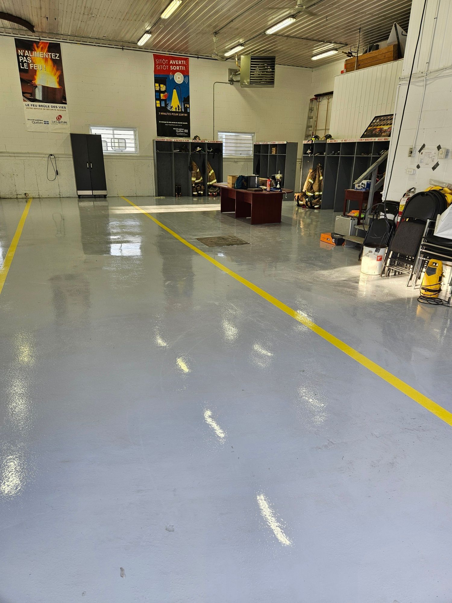 Interior of a workshop with gray floor, yellow lines, lockers, and equipment.