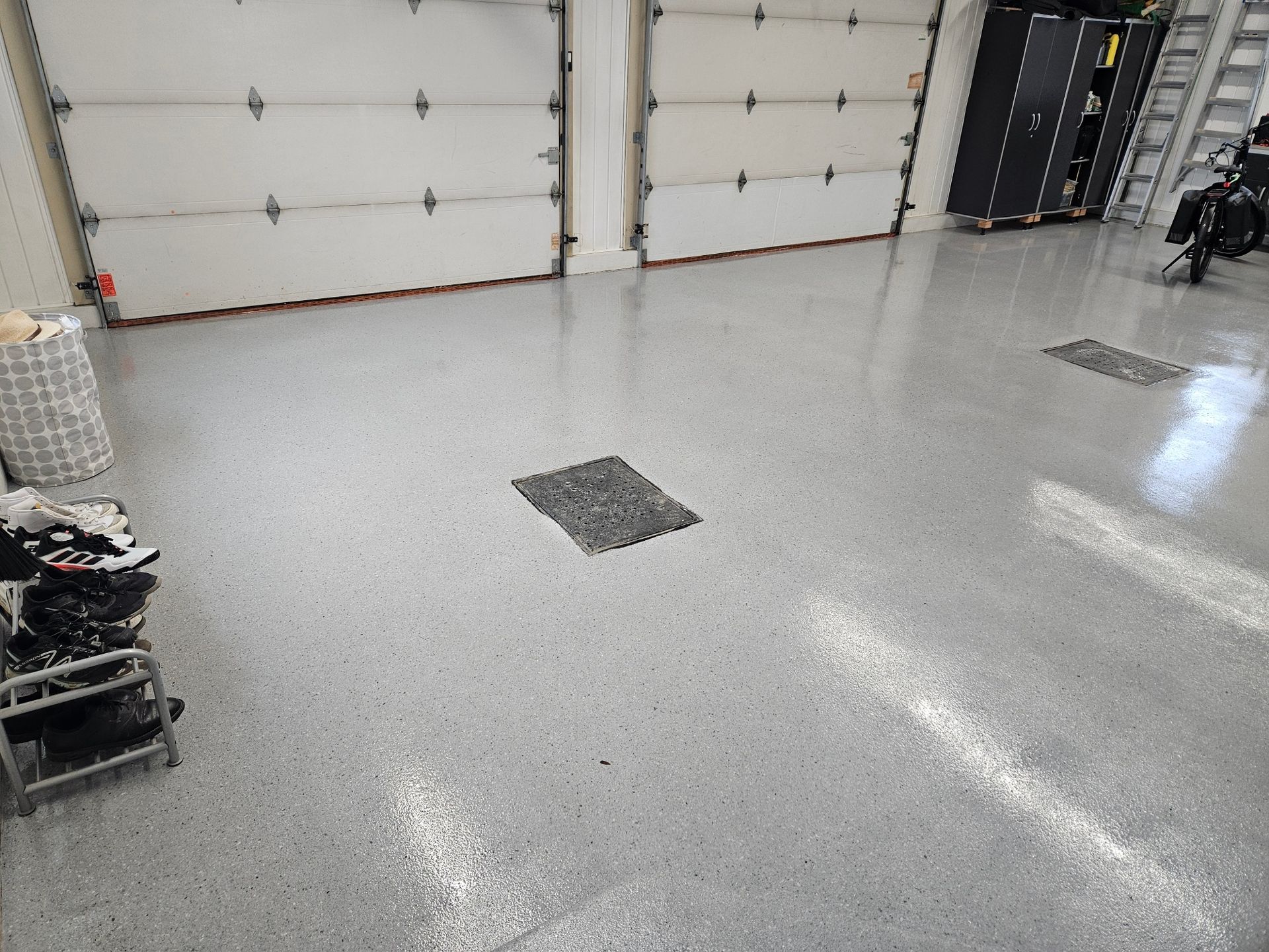 Garage with gray speckled epoxy floor, two white garage doors, a small mat, and a motorcycle.