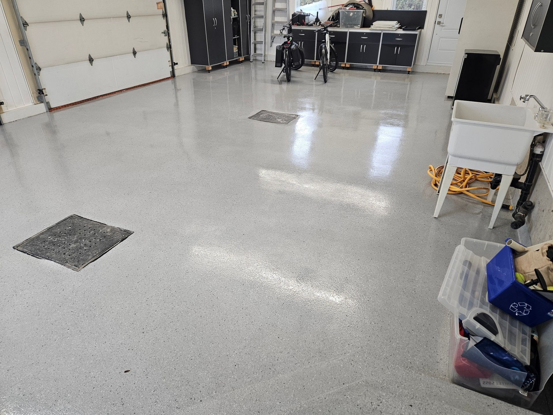Spacious garage with a speckled gray epoxy floor, a white utility sink, and various storage containers.