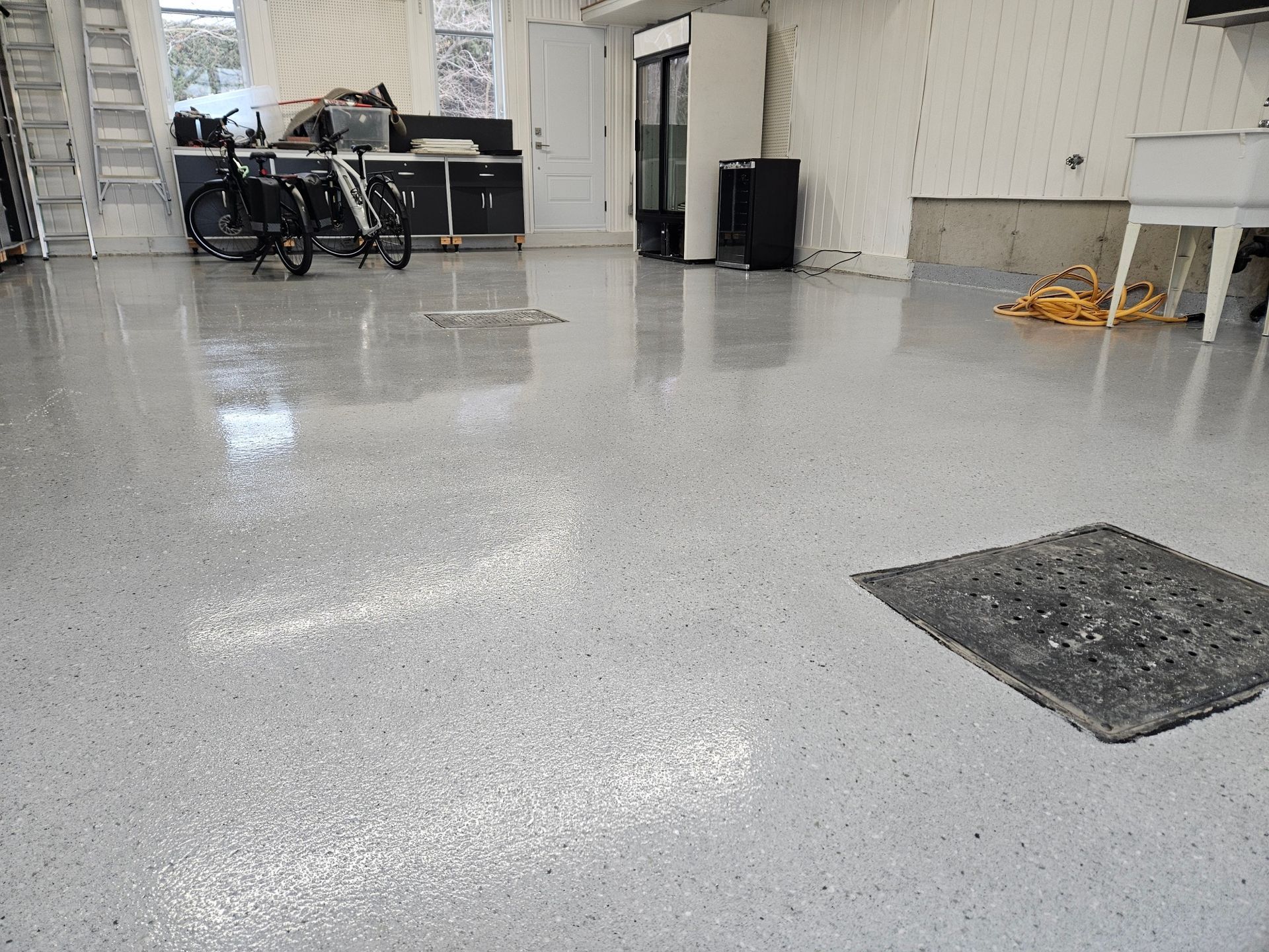 Light gray epoxy garage floor with bikes, cabinets, and a utility sink.
