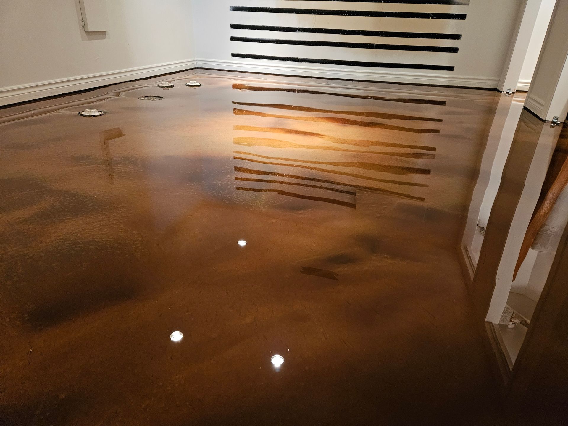 Glossy, metallic-bronze epoxy floor reflecting a black and white striped artwork in a gallery space.