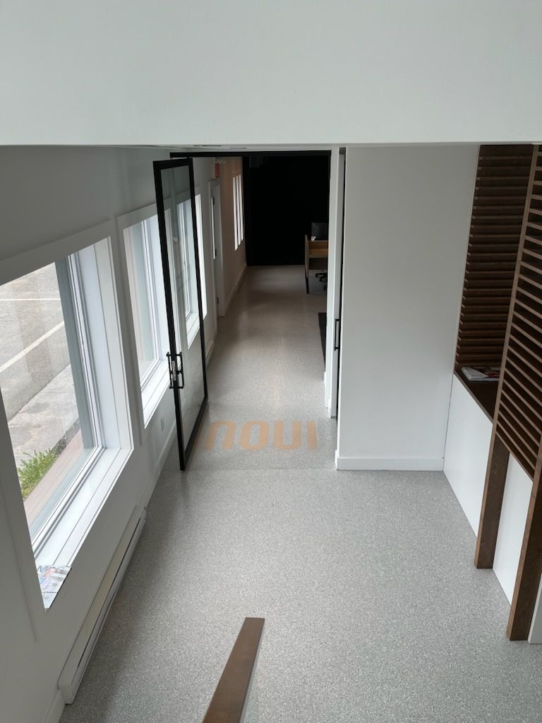 Hallway with windows on the left, open door, and wooden slats on the right. Light terrazzo flooring.
