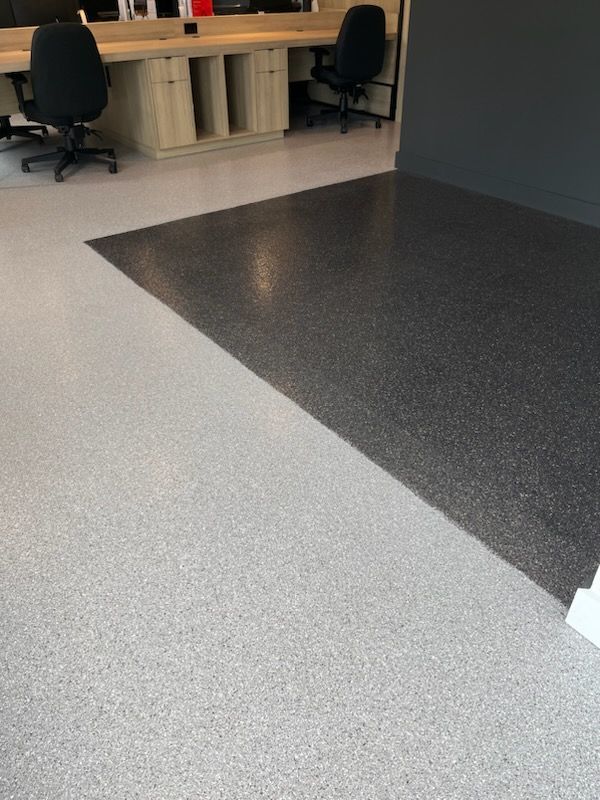 Gray and black speckled flooring in an office, contrasting colors. Desks and chairs in background.