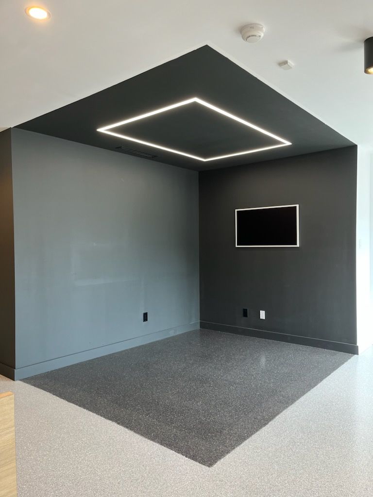 Empty room with gray walls and flooring, dark gray accent ceiling, lit square. TV on the wall.
