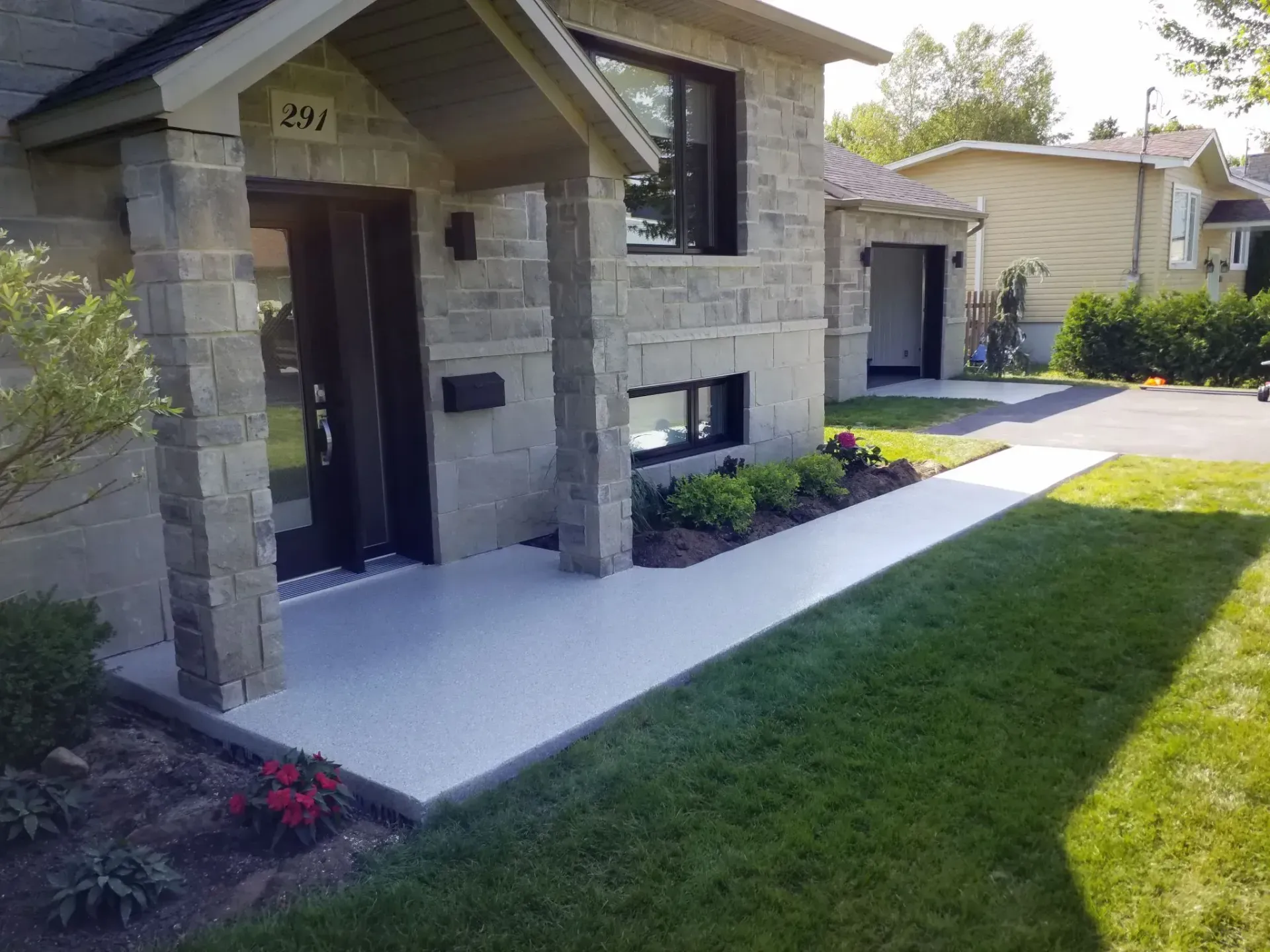 Gray stone house with a covered entryway, black door, and a walkway alongside green grass.