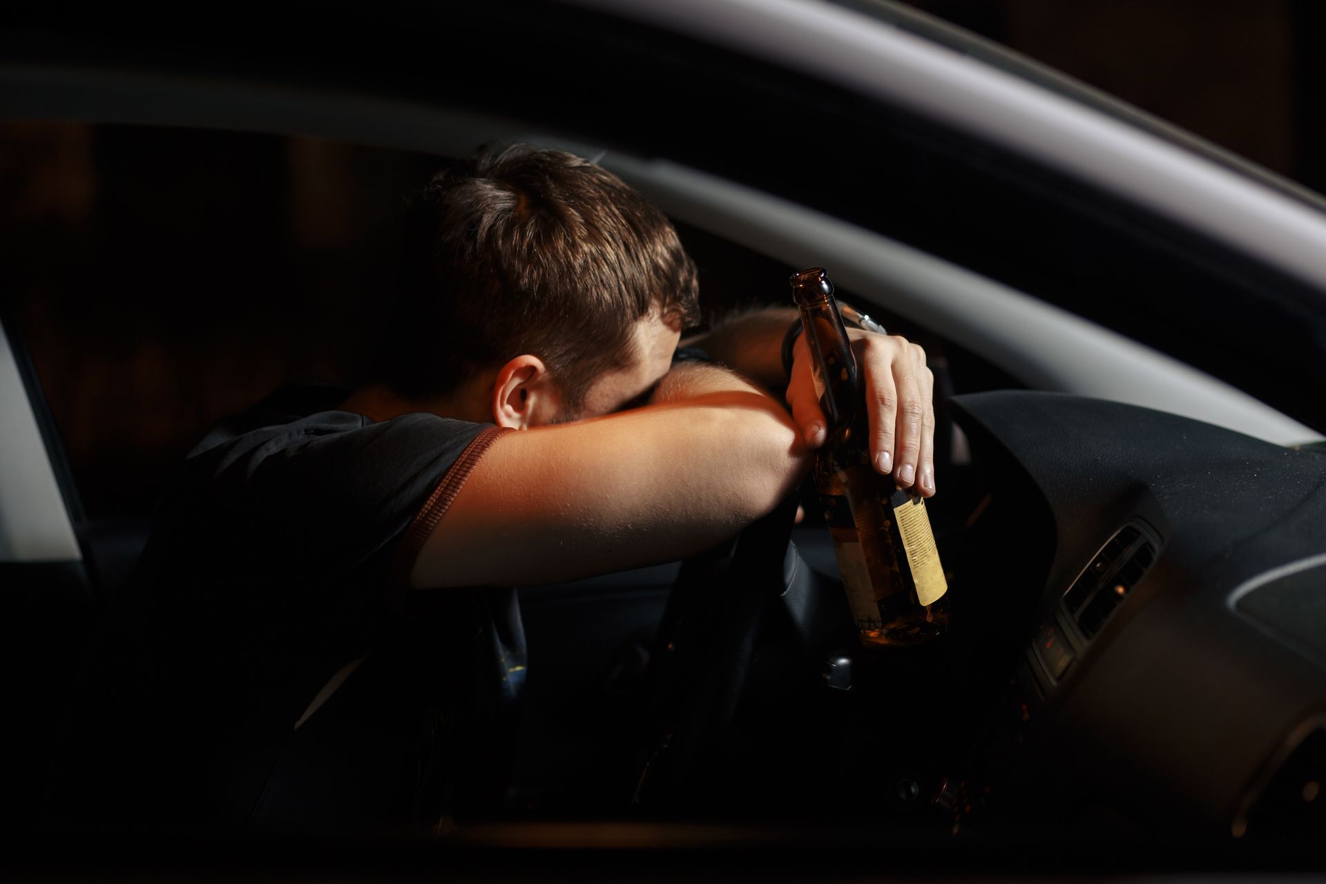 Man slumped over steering wheel, holding a beer bottle in car. DUI in Florida.