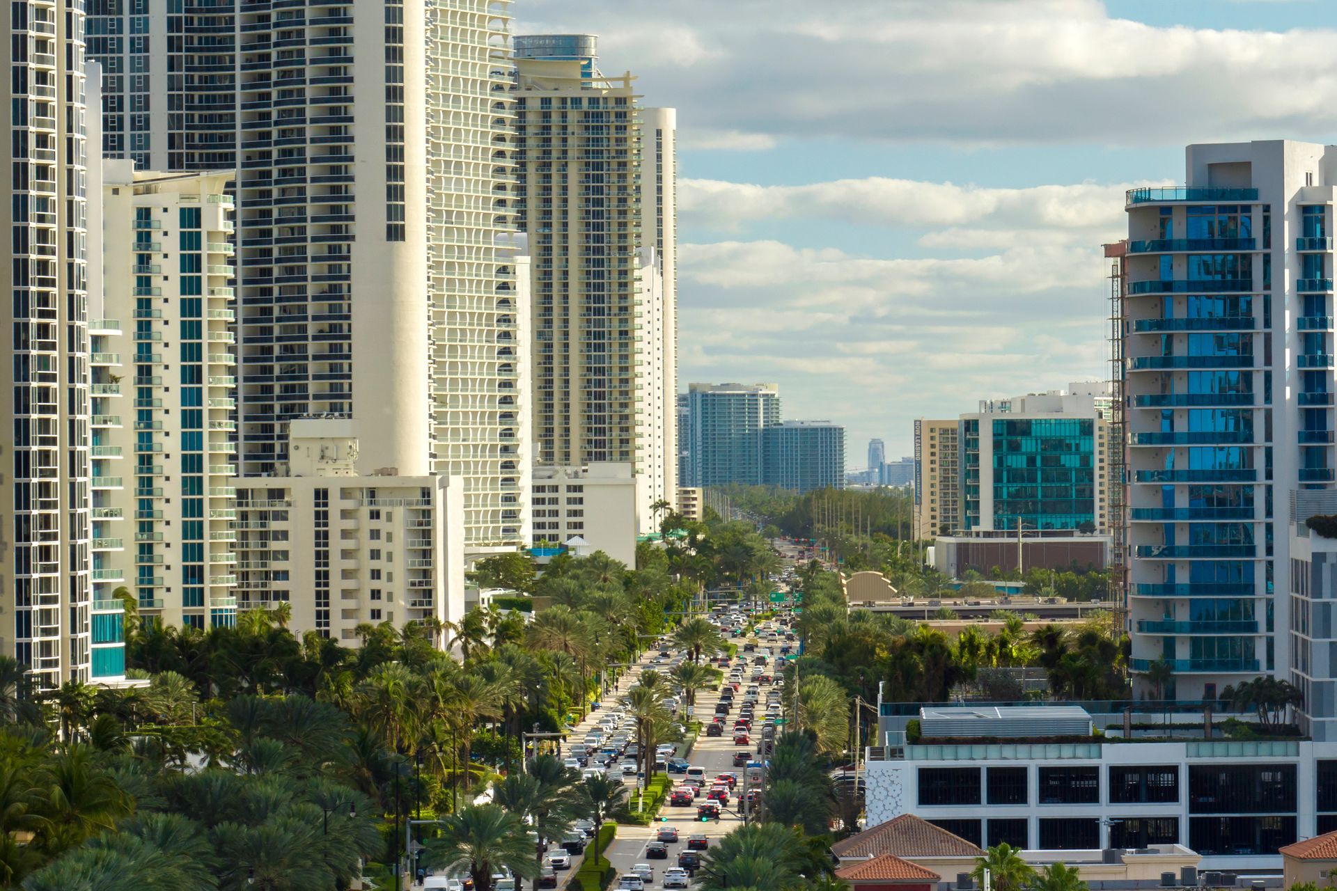 High-rise buildings line a street with traffic, under a cloudy sky.