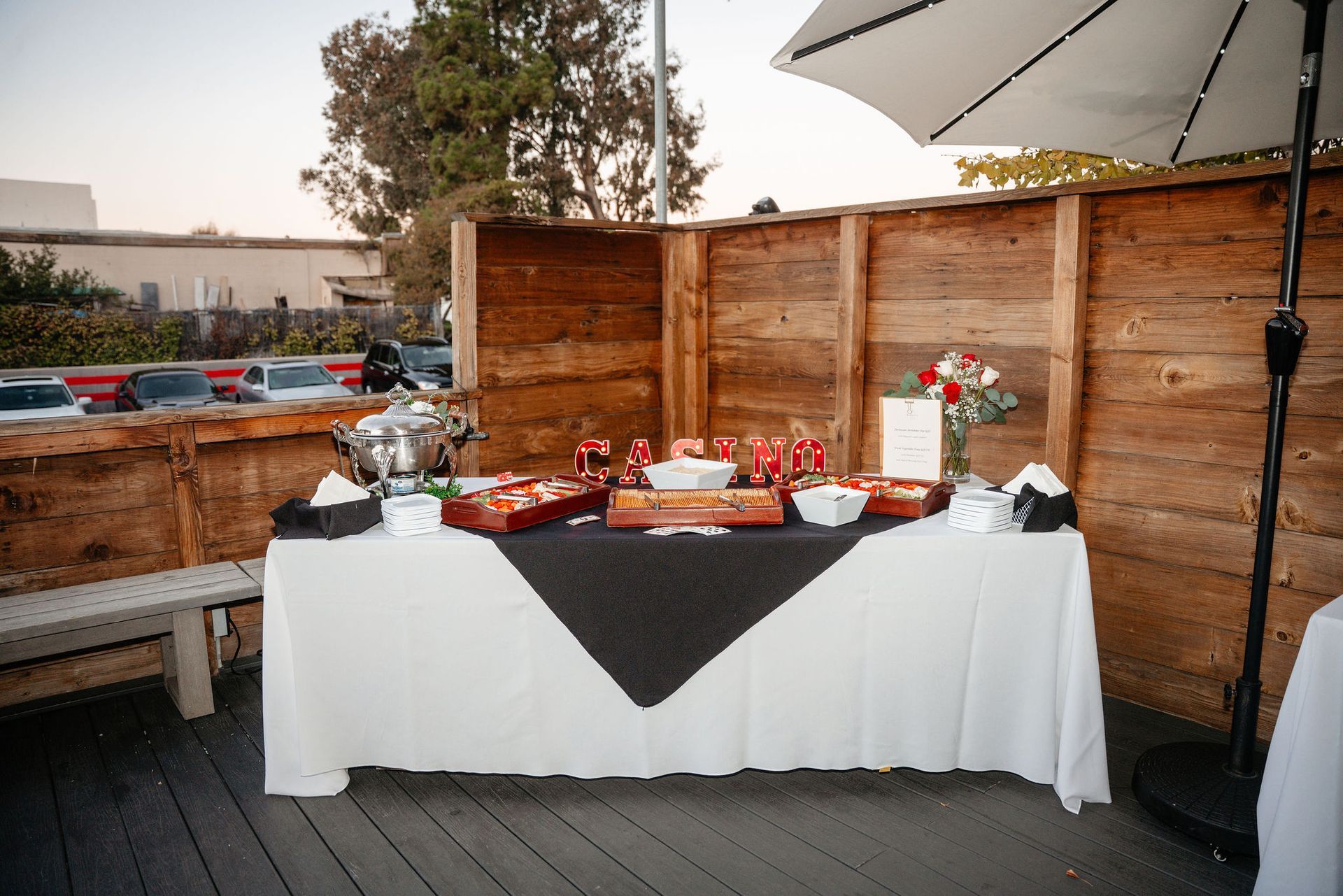 Buffet table with snacks and drinks outdoors, against a wooden fence.