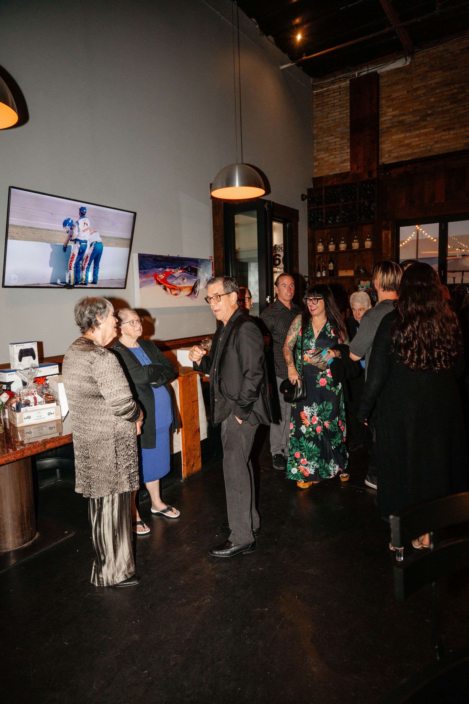 People socializing in a dimly lit restaurant. A TV screen displays a photograph; dark wooden elements are visible.