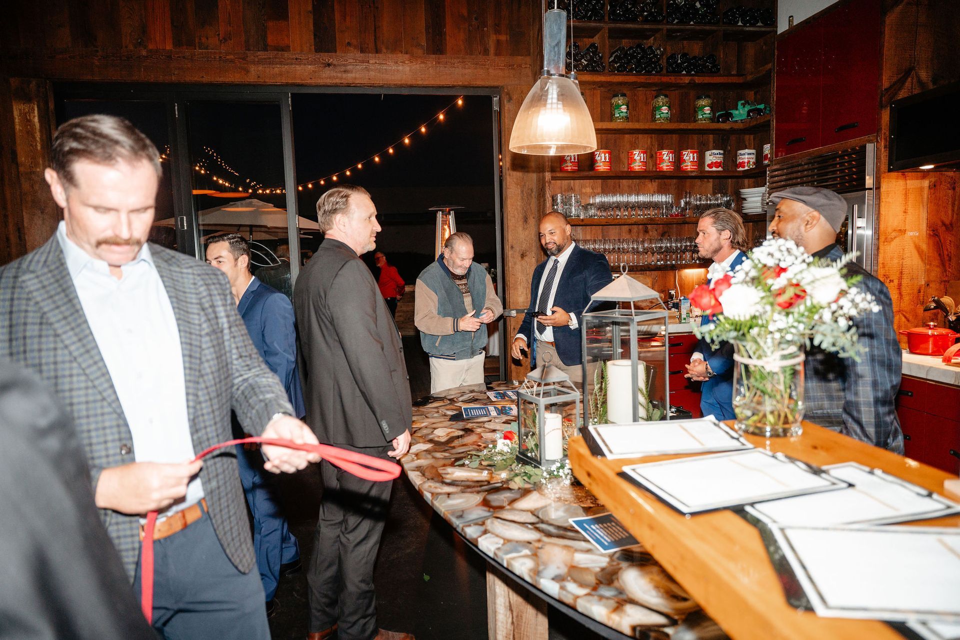 Group of men at a bar, some holding drinks, a few looking at a menu. Interior, warm lighting.