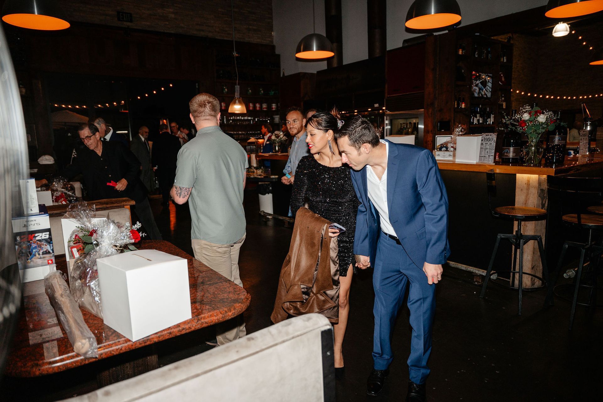 People socializing in a dimly lit bar, a couple walking together, some holding hands.