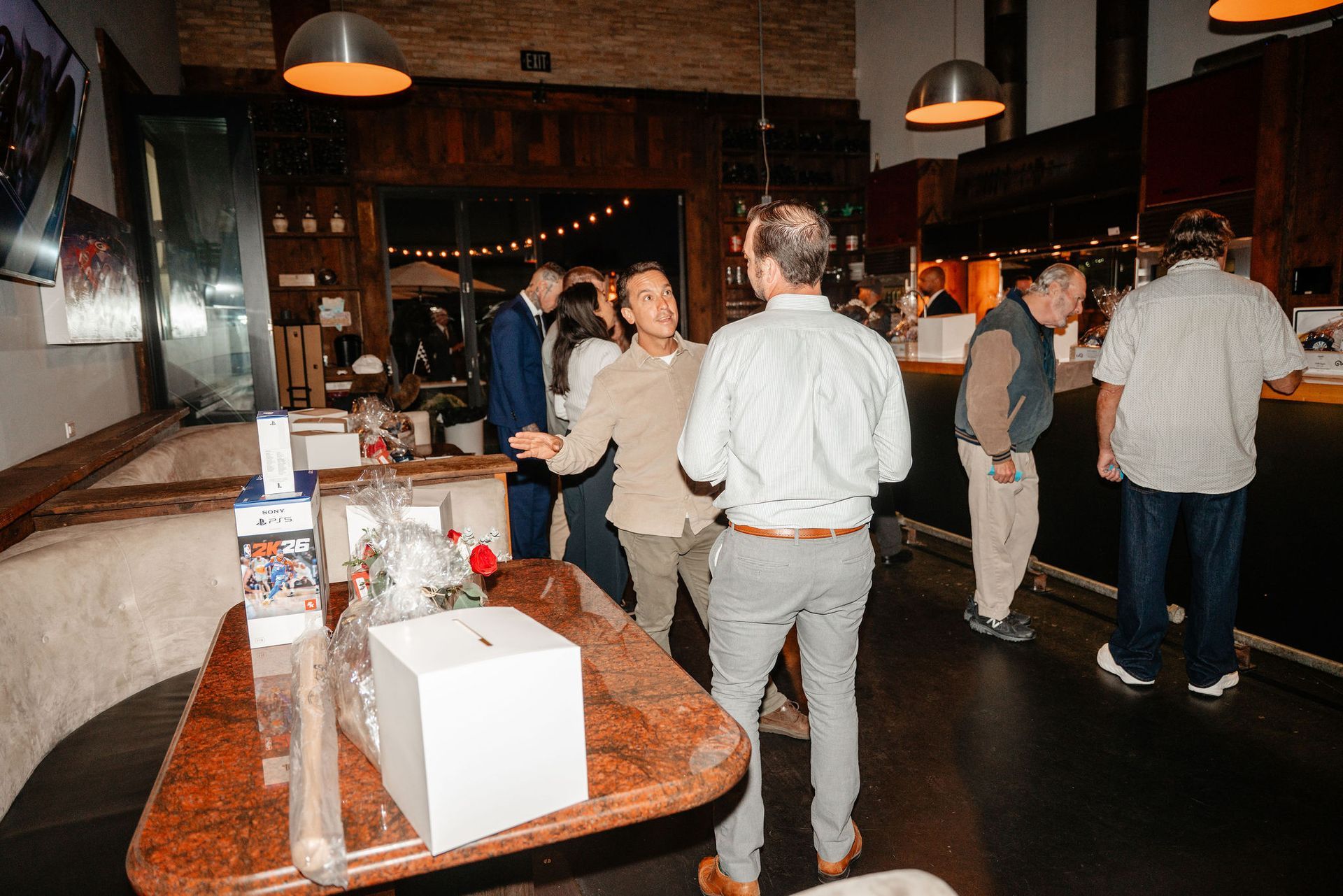 People socializing in a bar; some are near the bar, while others dance. Low lighting, wooden accents.