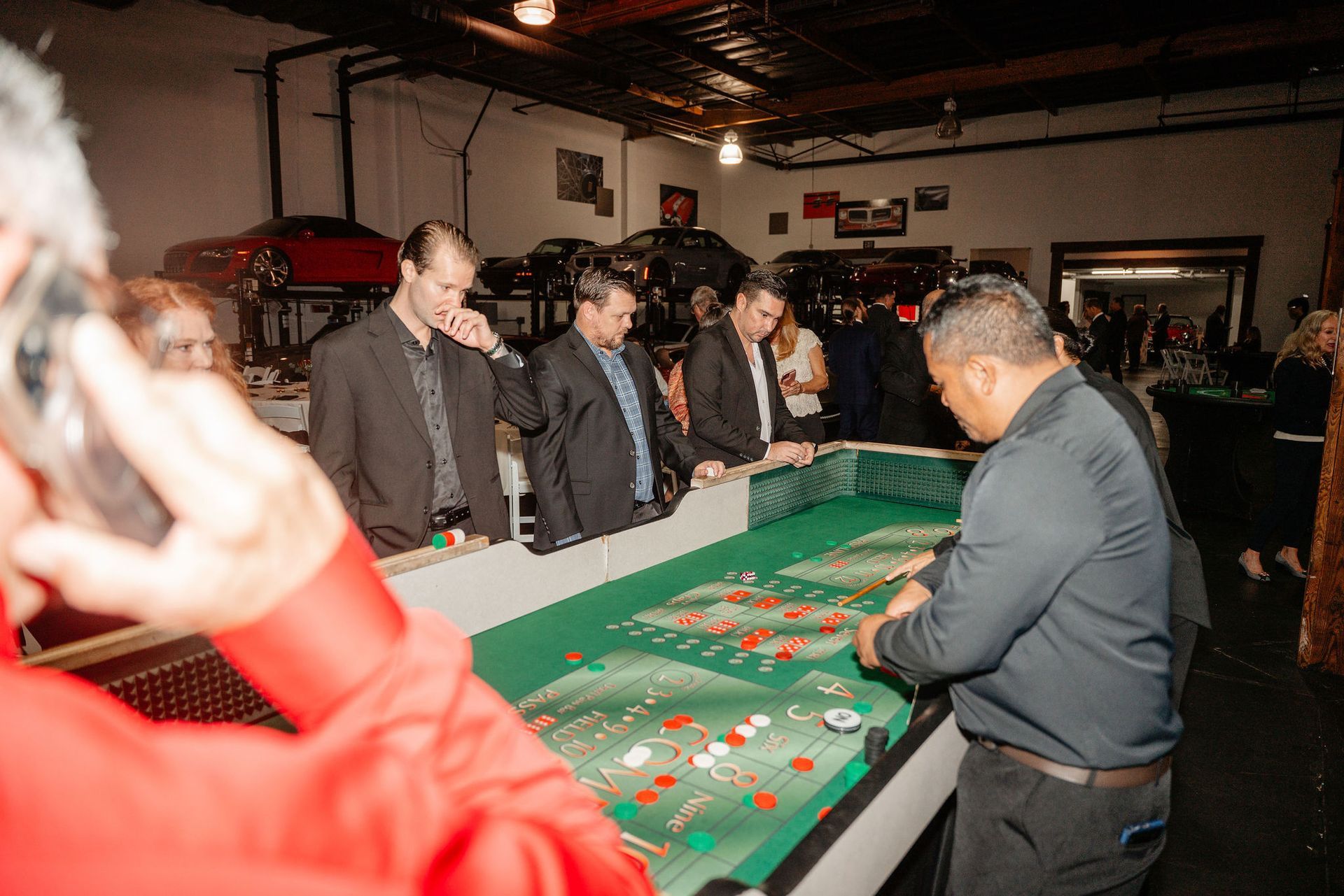 People playing roulette at an event. Men in suits surround the green felt table, a dealer manages the chips.