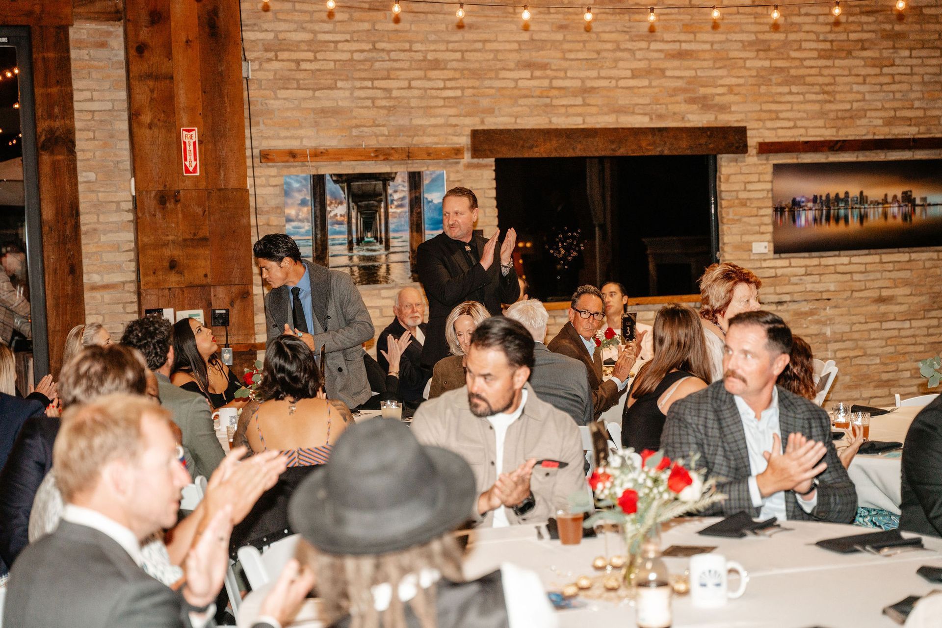 People clapping at a formal event, a man speaking in front of the crowd.