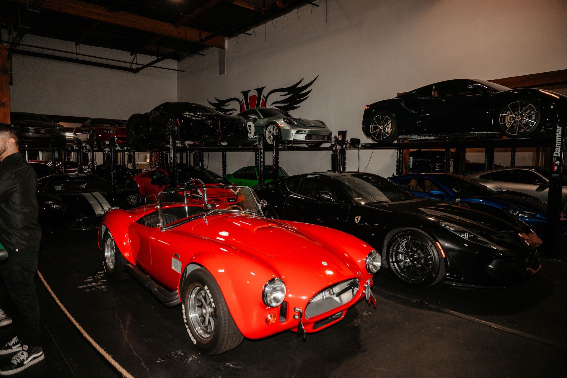 Red Cobra sports car in a garage filled with other cars, including black sports cars on lifts.
