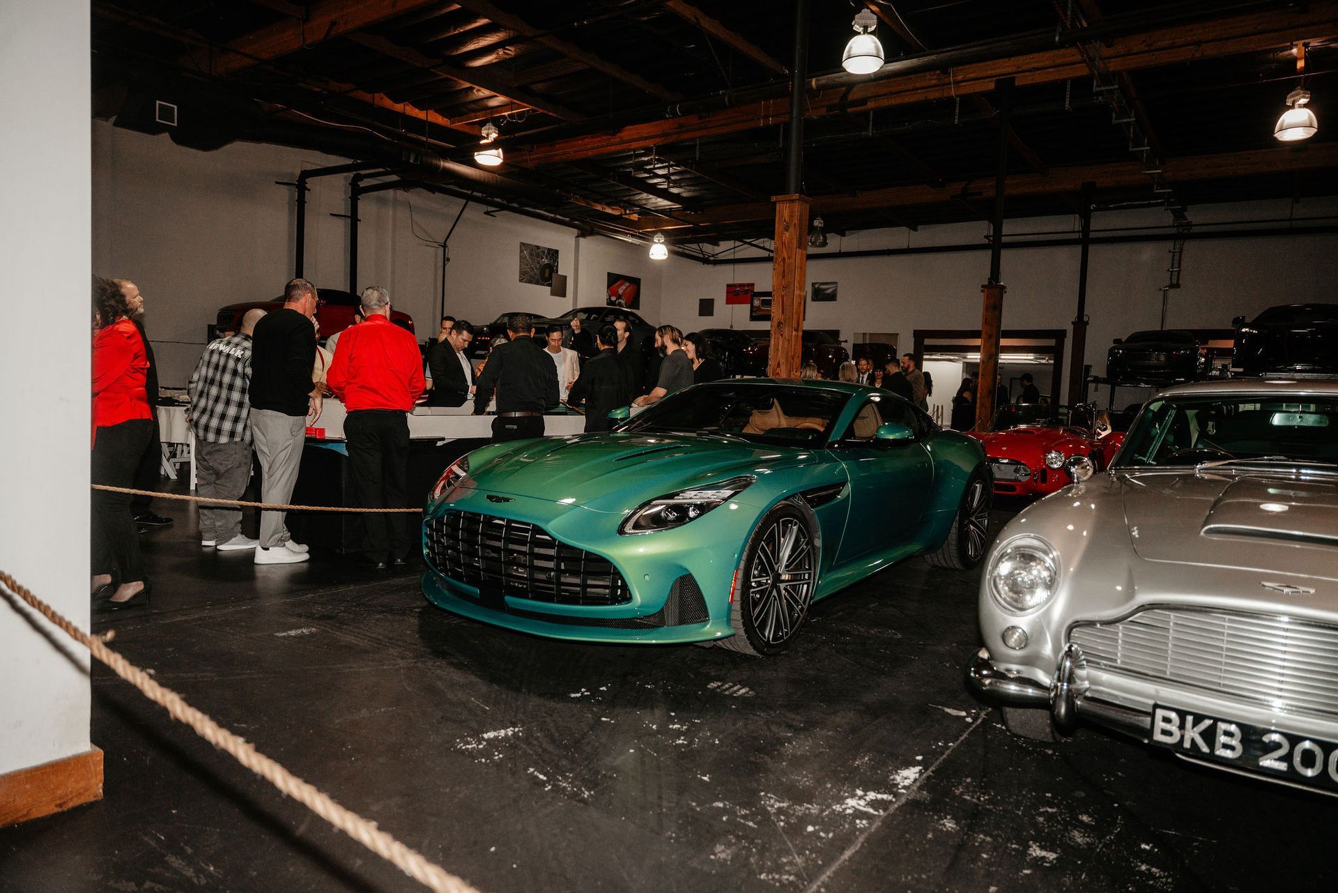 Green sports car on display at an event with people in an industrial-style setting.