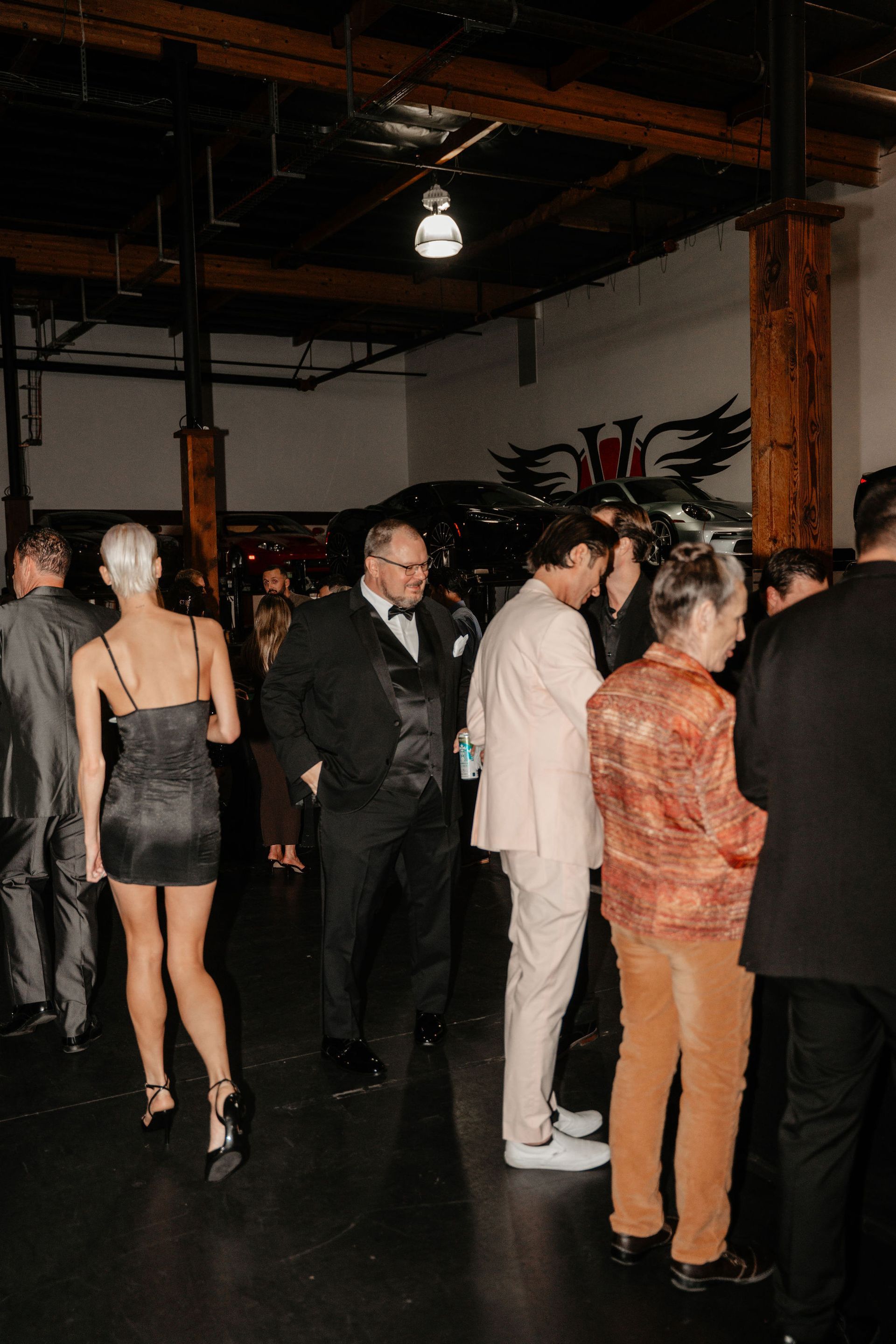 People in formal attire at an event in a large industrial-style space.