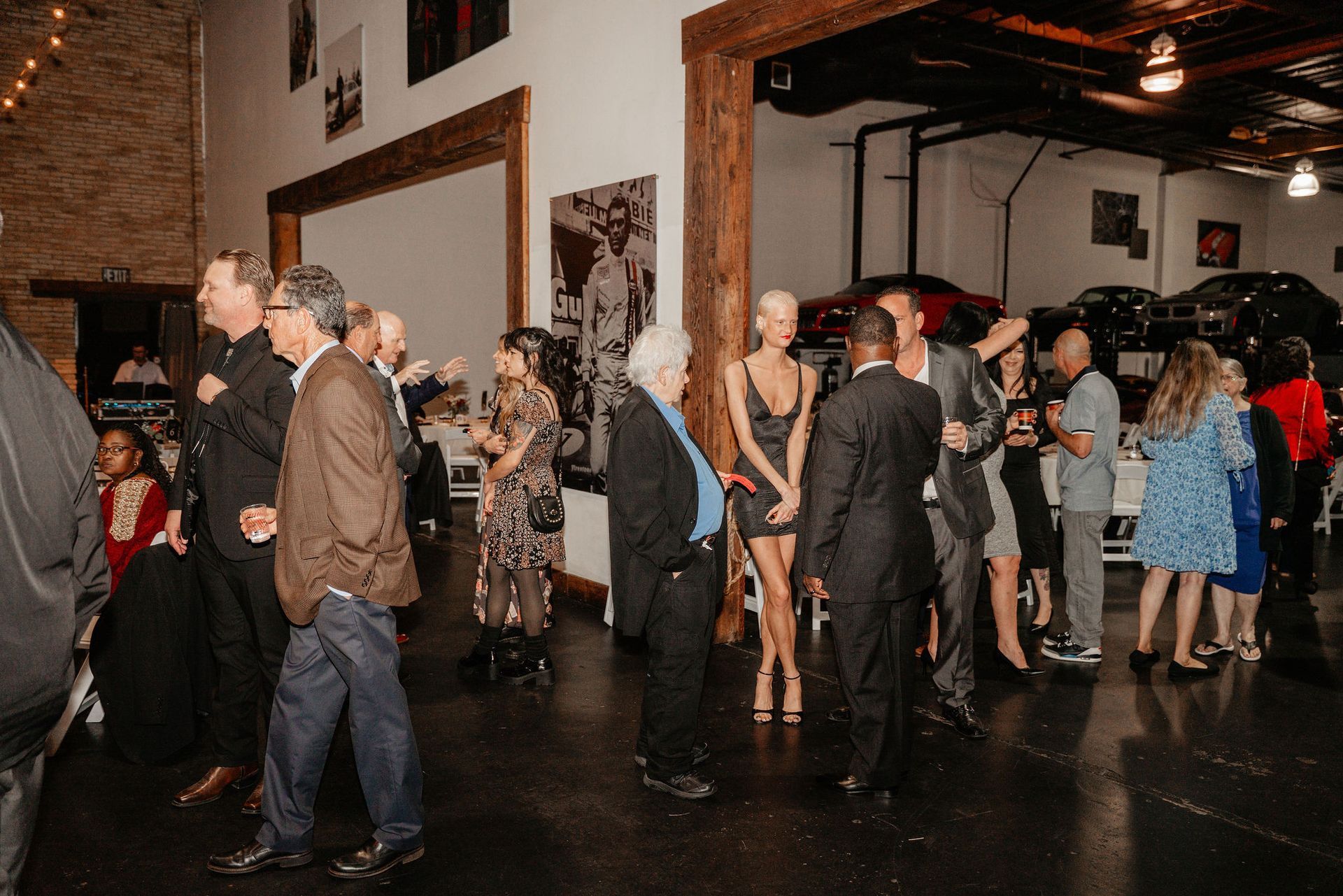 People socializing at an event in a large, open space with art on the walls and cars visible in the background.