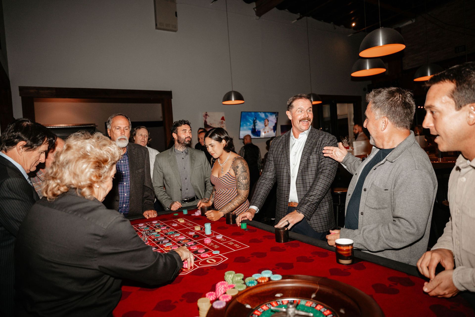 People around a casino roulette table; red felt, chips, and animated discussion.