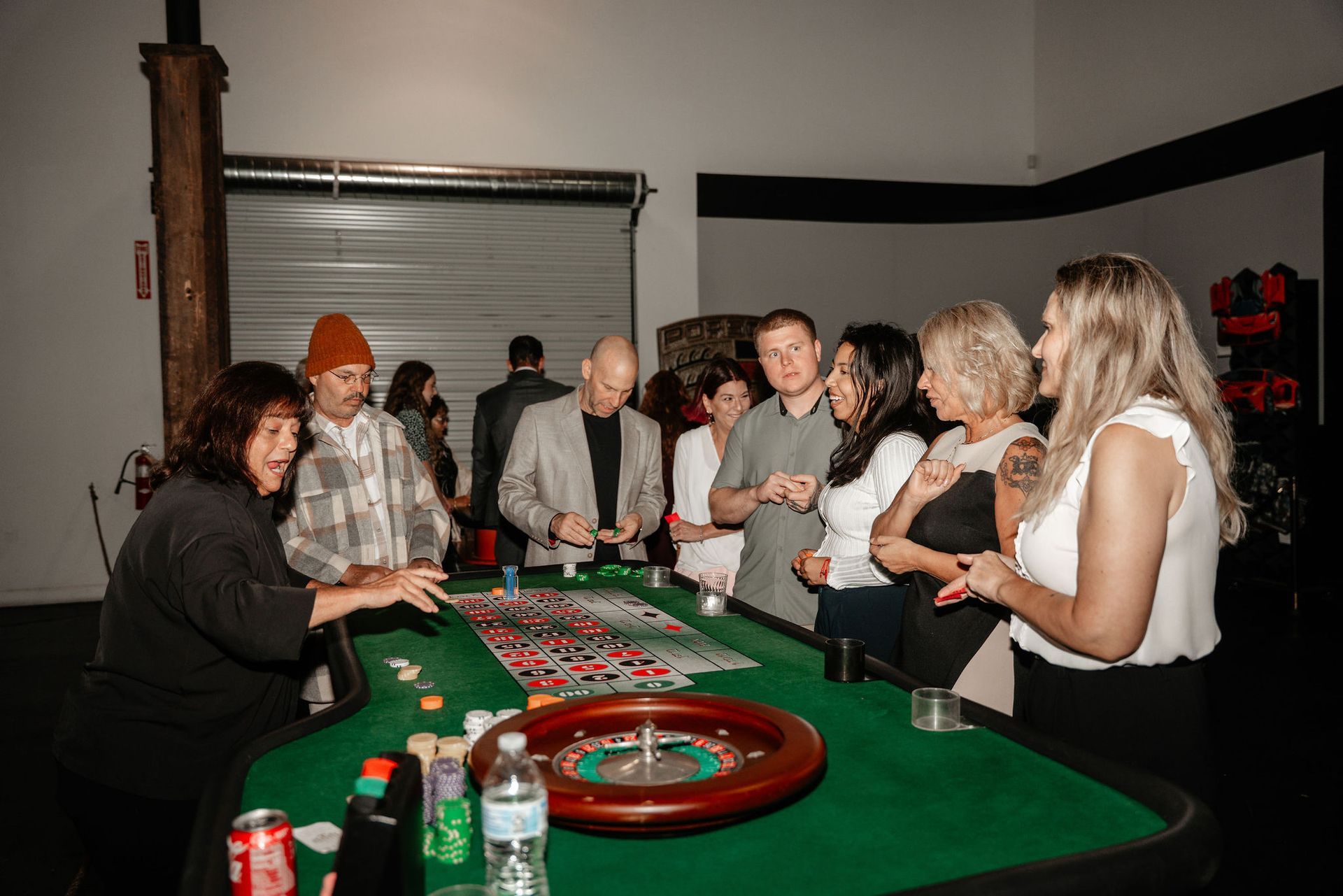 People gathered around a roulette table in a dimly lit room, some placing bets and watching the game.
