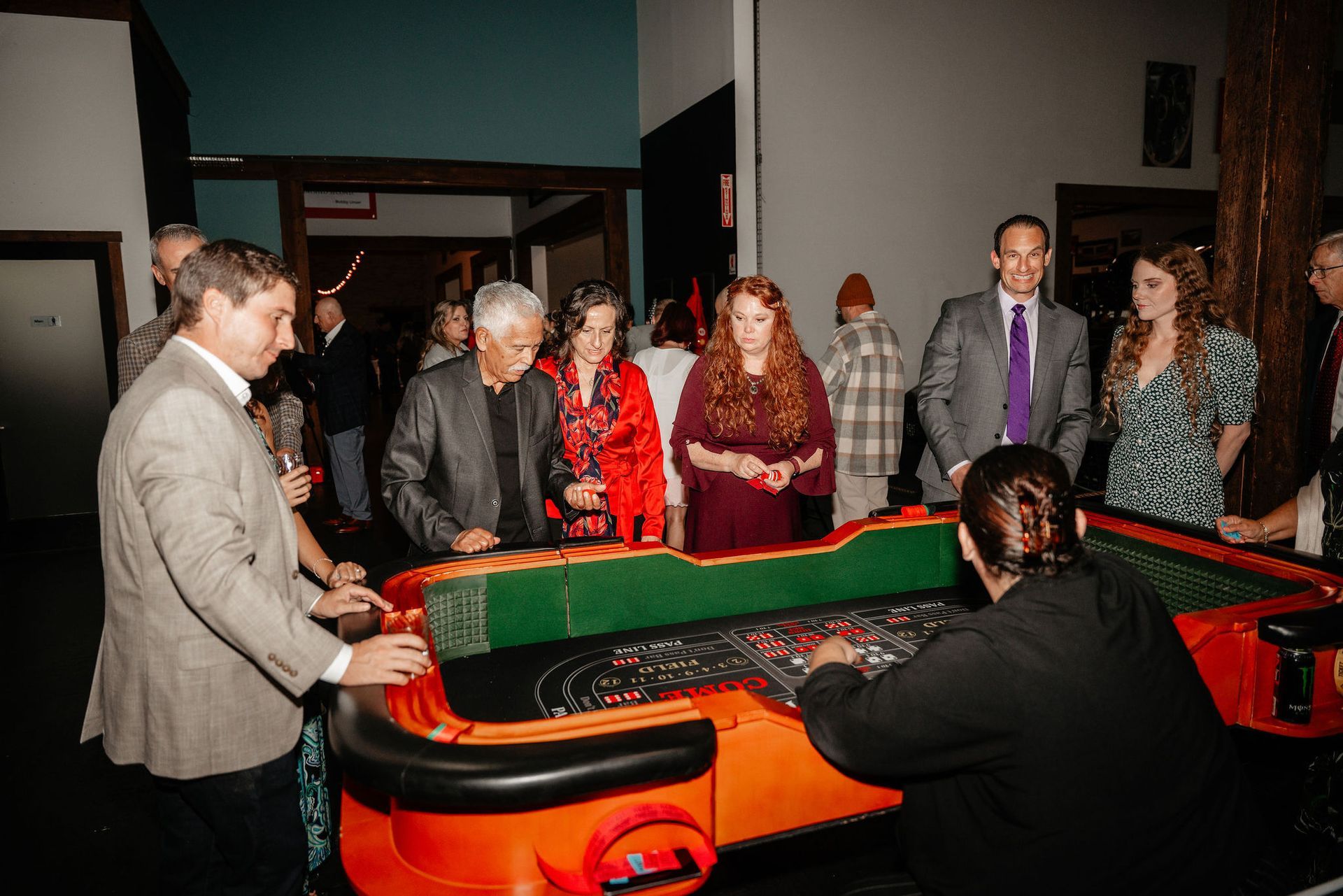 People playing at a roulette table in a dimly lit room. A dealer stands behind the table.
