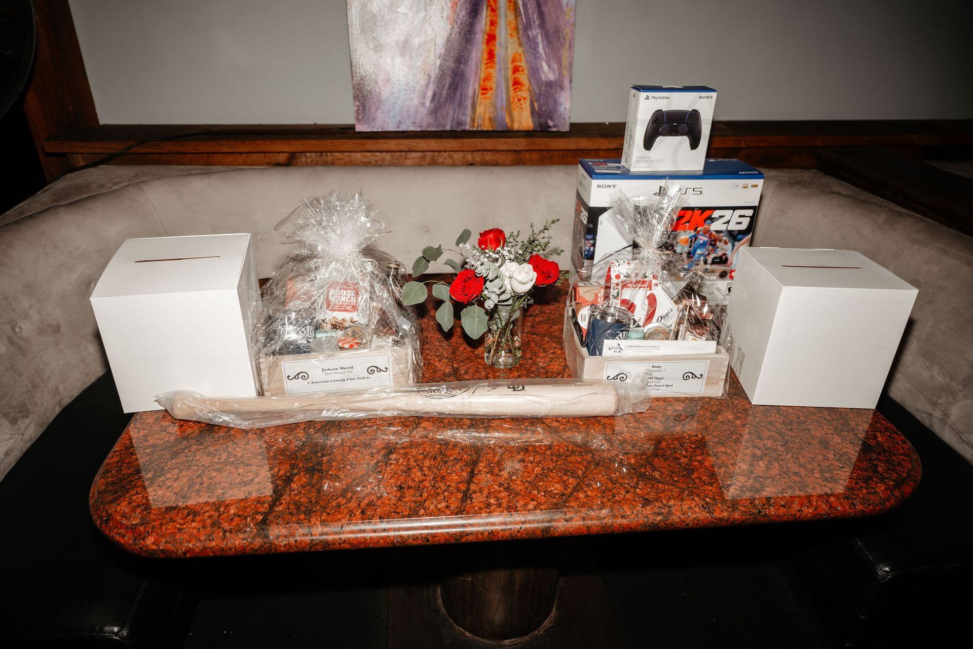 Display of gifts: two gift baskets, a video game console, controller, and flowers, on a decorative table.