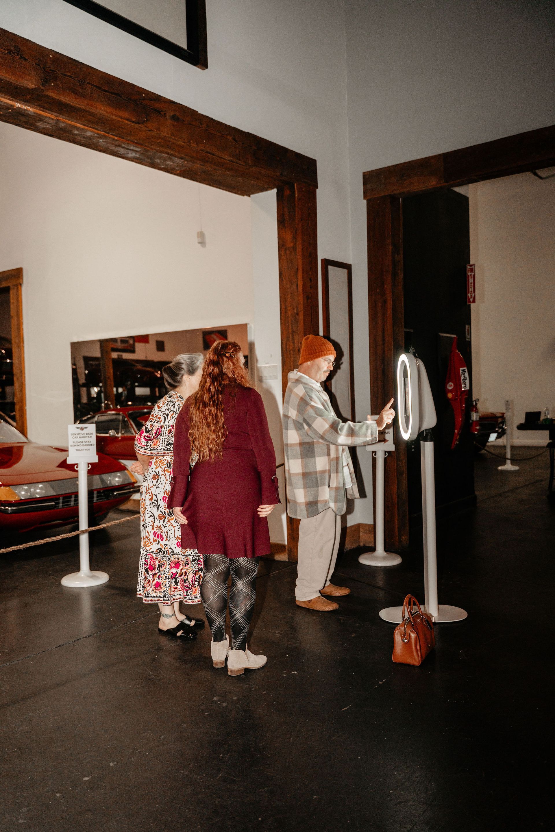 People at kiosk in museum, looking at a display next to an old red car.