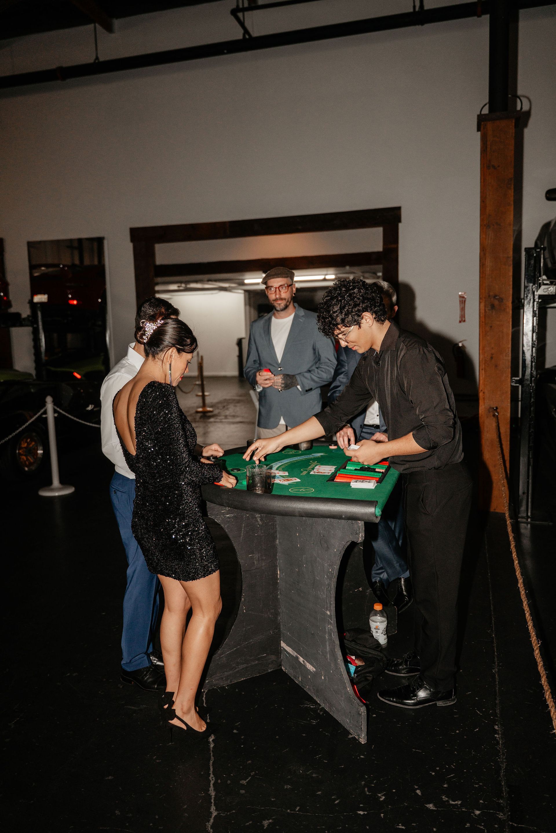 People playing cards at a casino table indoors. One woman in a sequin dress, a man in a suit, a dealer.