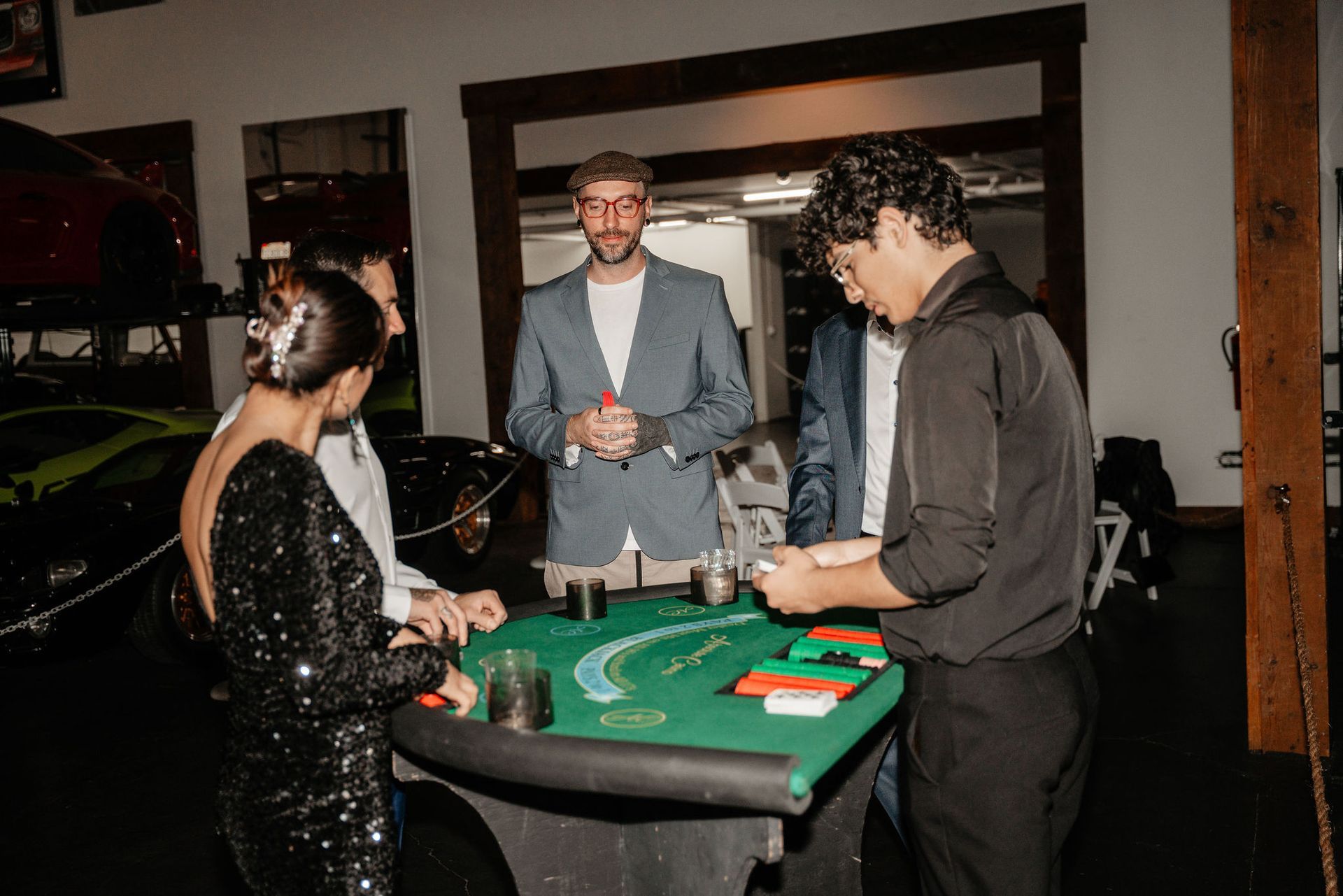 People playing blackjack at a table in a garage. Several cars are visible in the background.
