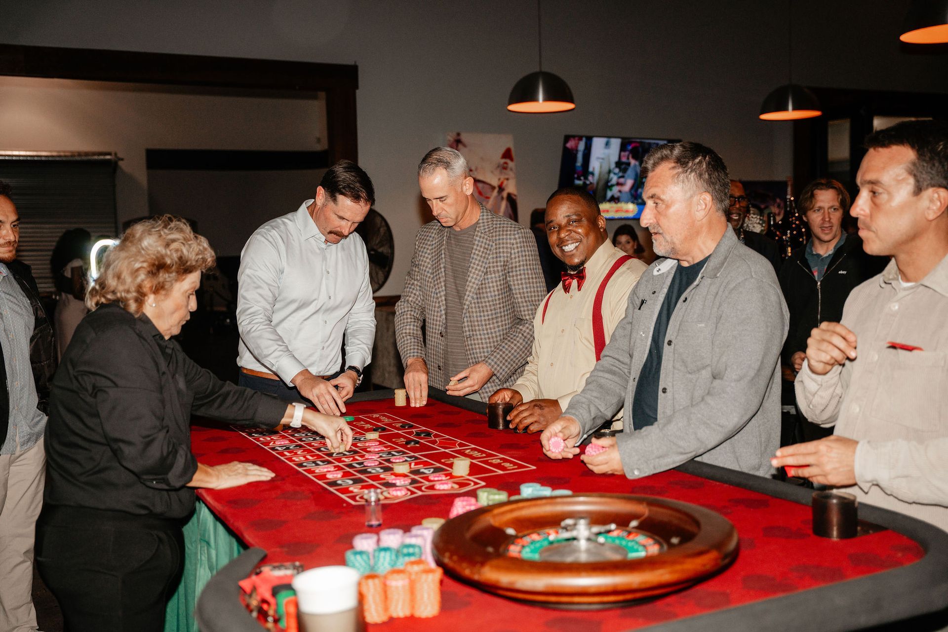 People playing roulette at a casino table. The table is red with colored chips and a spinning wheel.