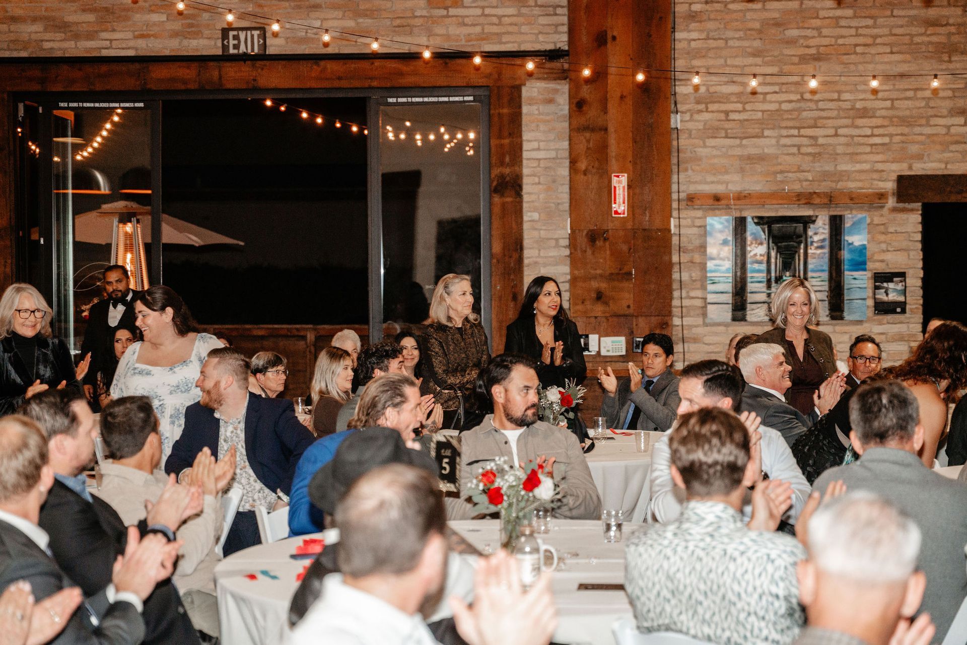 People applauding as speakers address them at an event in a warmly lit venue.