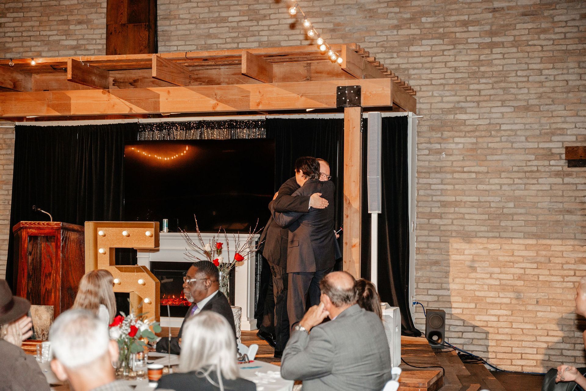 Two men in suits embrace onstage at an event with a 