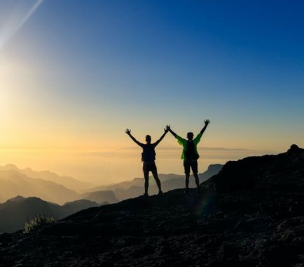 Two people are standing on top of a mountain with their arms in the air.