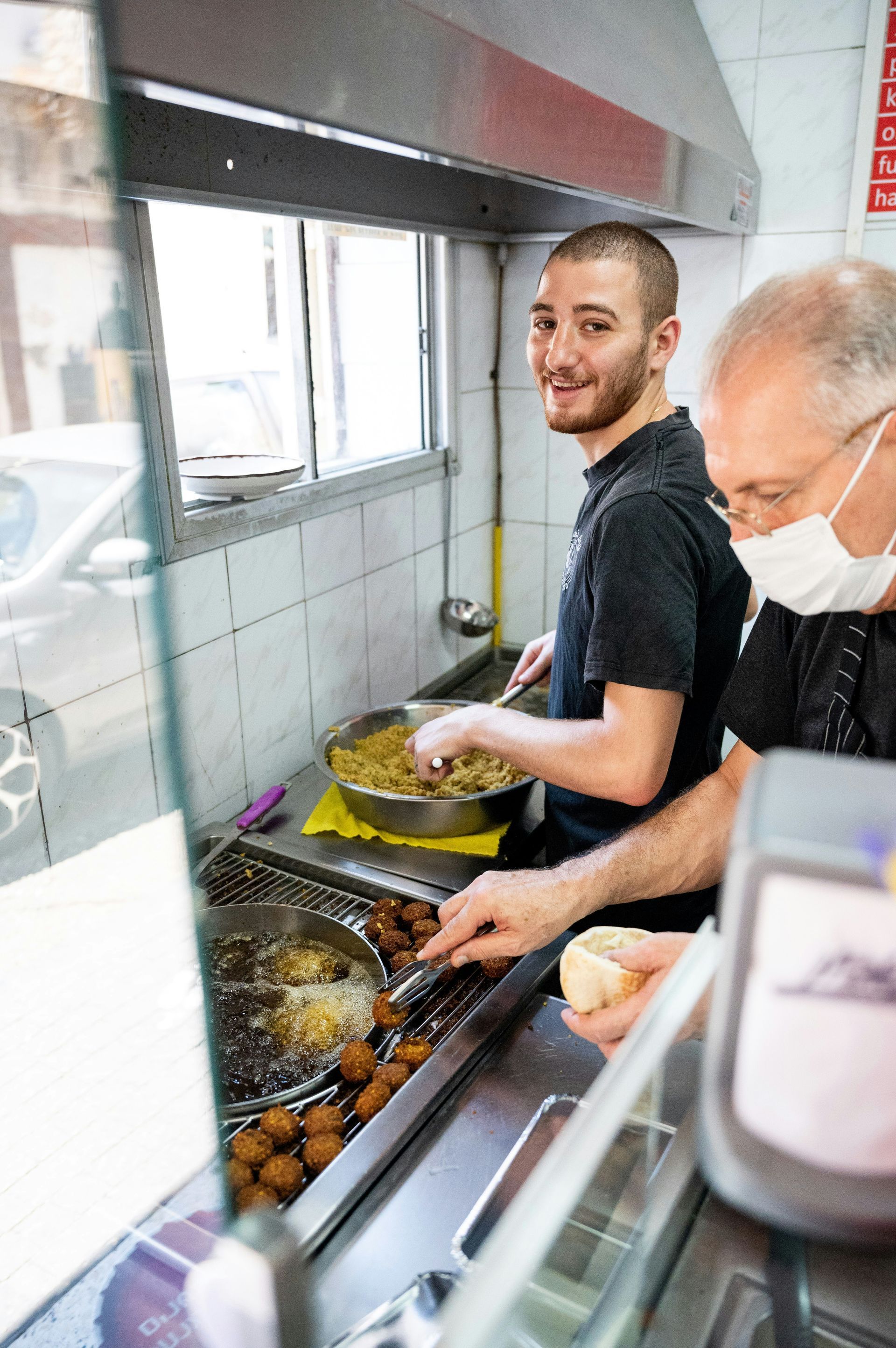 Two men wearing face masks are cooking food in a kitchen.