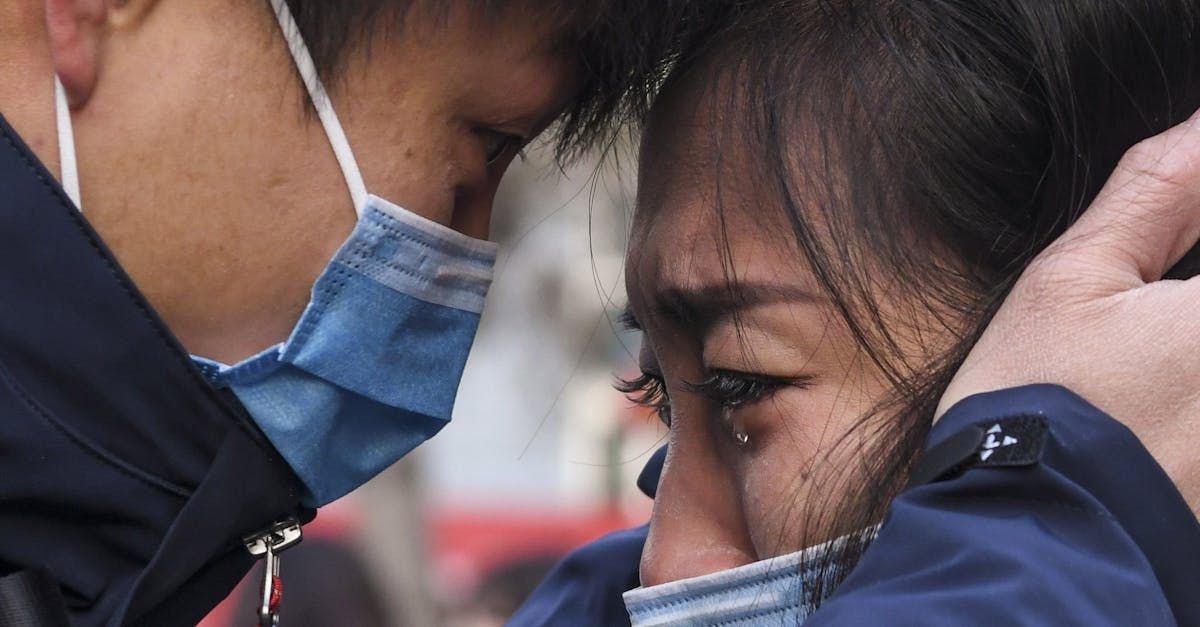 A man and a woman wearing face masks are hugging each other.