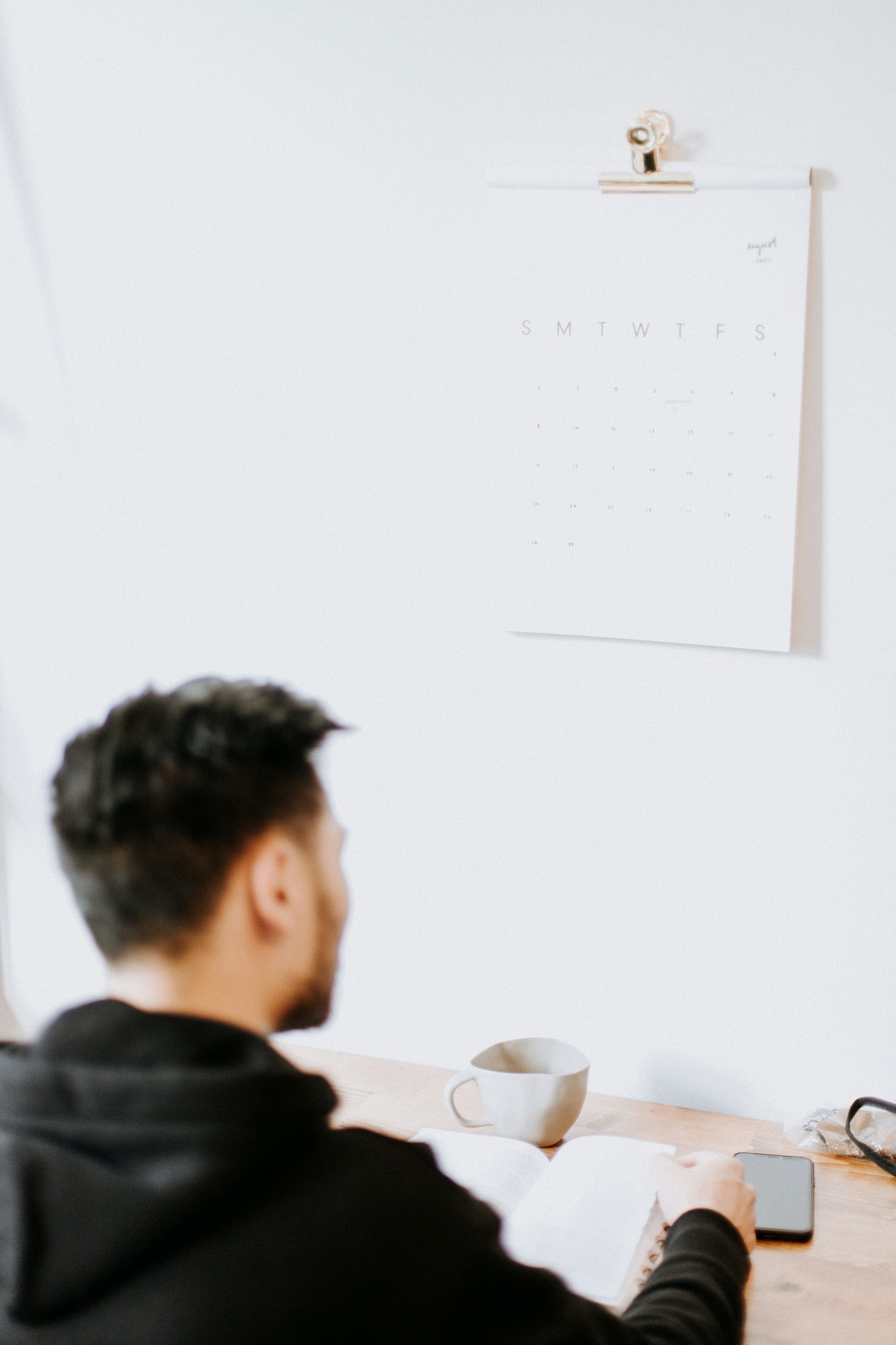 A man is sitting at a desk with a cup of coffee and a book.