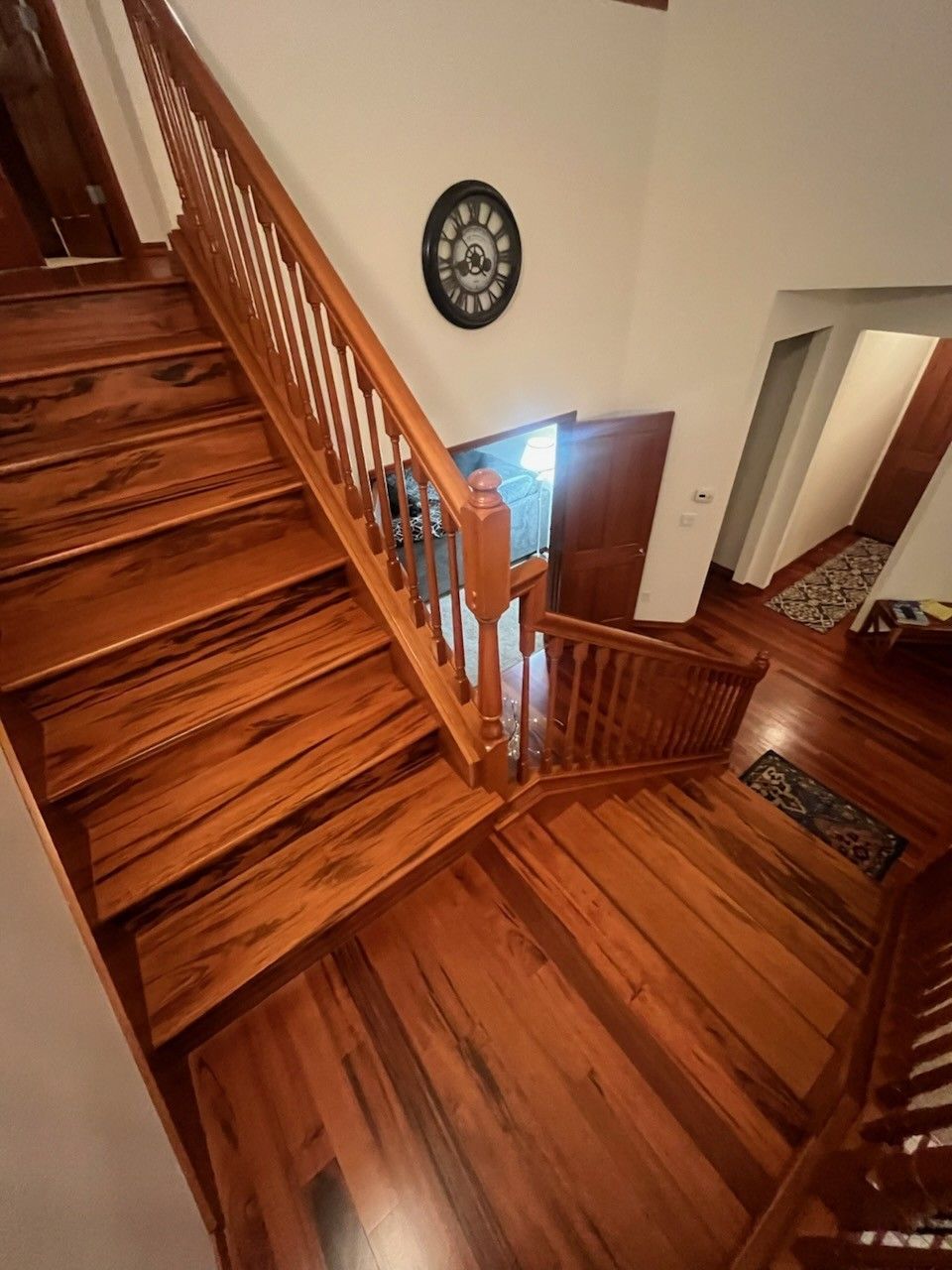 Interior view of a wooden staircase with a dark wood railing, leading up to a second floor.