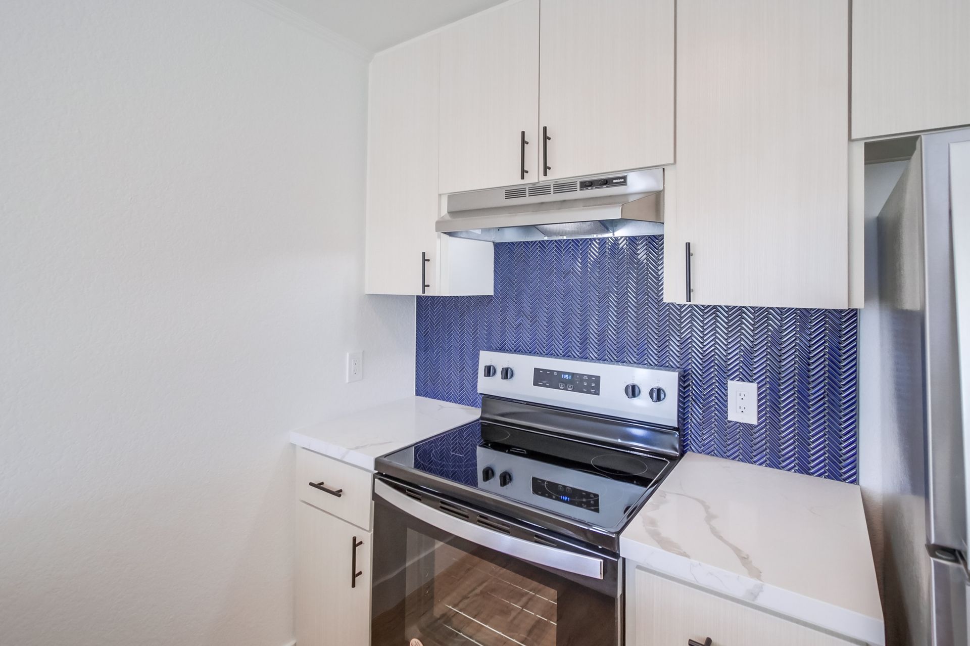 Kitchen with blue backsplash, white cabinets, stainless steel stove, and white countertops.